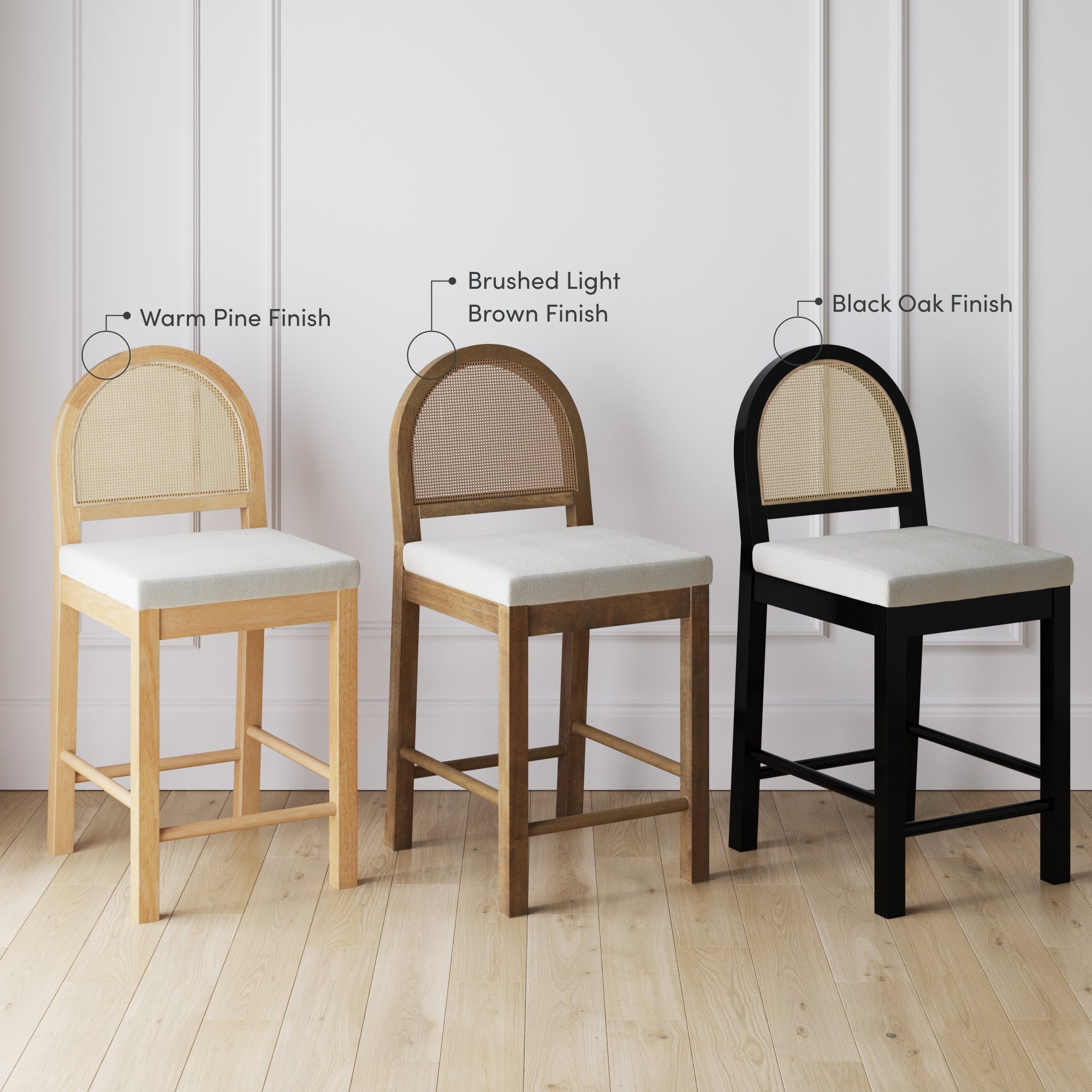 Three wooden chairs with cushioned seats placed side by side, each with a different frame finish: warm pine, brushed light brown, and black oak, against a white paneled wall on a light wood floor.
