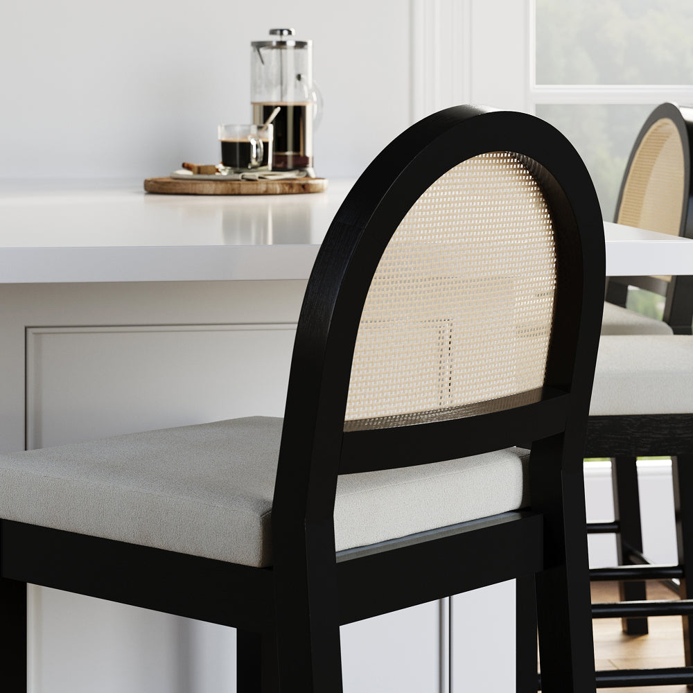 Black bar stool with an arched cane backrest and a light gray upholstered seat, positioned at a white kitchen counter.