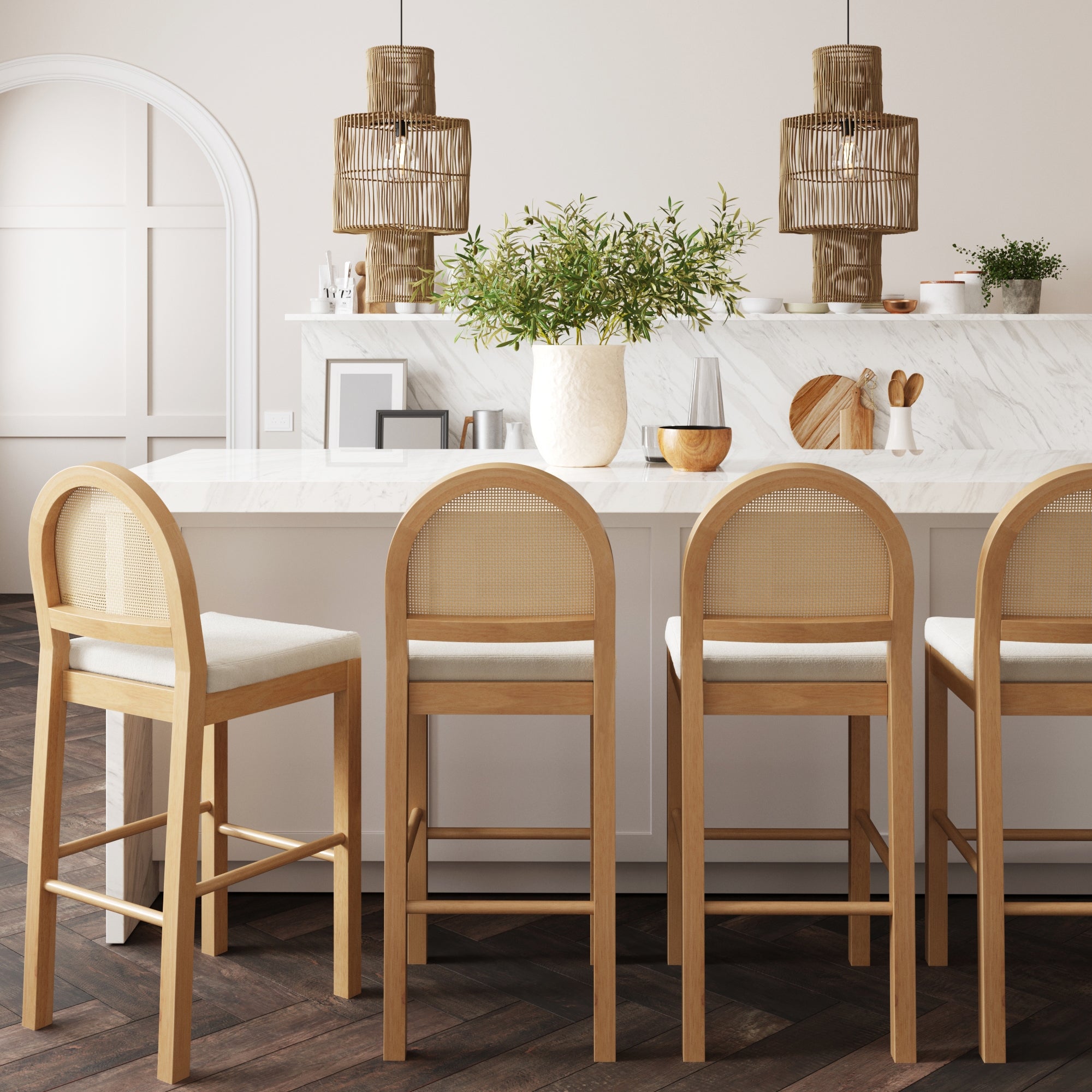 A modern kitchen with a white marble island, four light wood and cane barstools, potted plant centerpiece, arched door, and hanging rattan pendant lights over the counter.