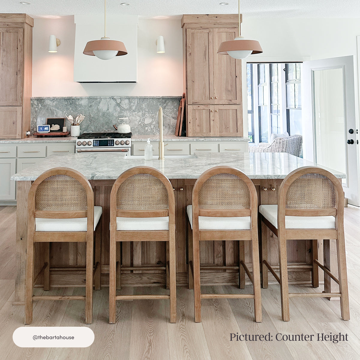 Four Nathan James Boucle Bar Stools Light Brown with rounded natural rattan backs and white boucle fabric seats arranged in a row at a kitchen island.
