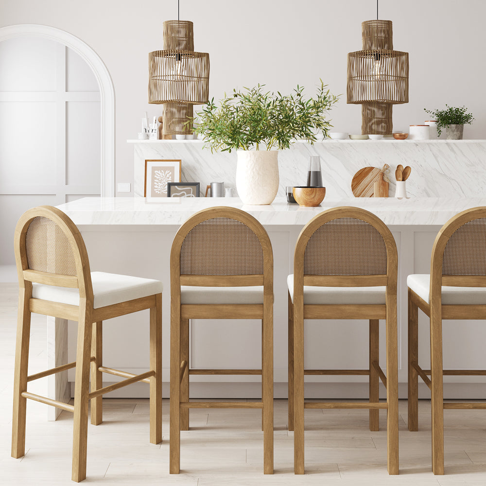 Four wooden bar stools with arched, cane-back seats lined up at a white marble kitchen island.