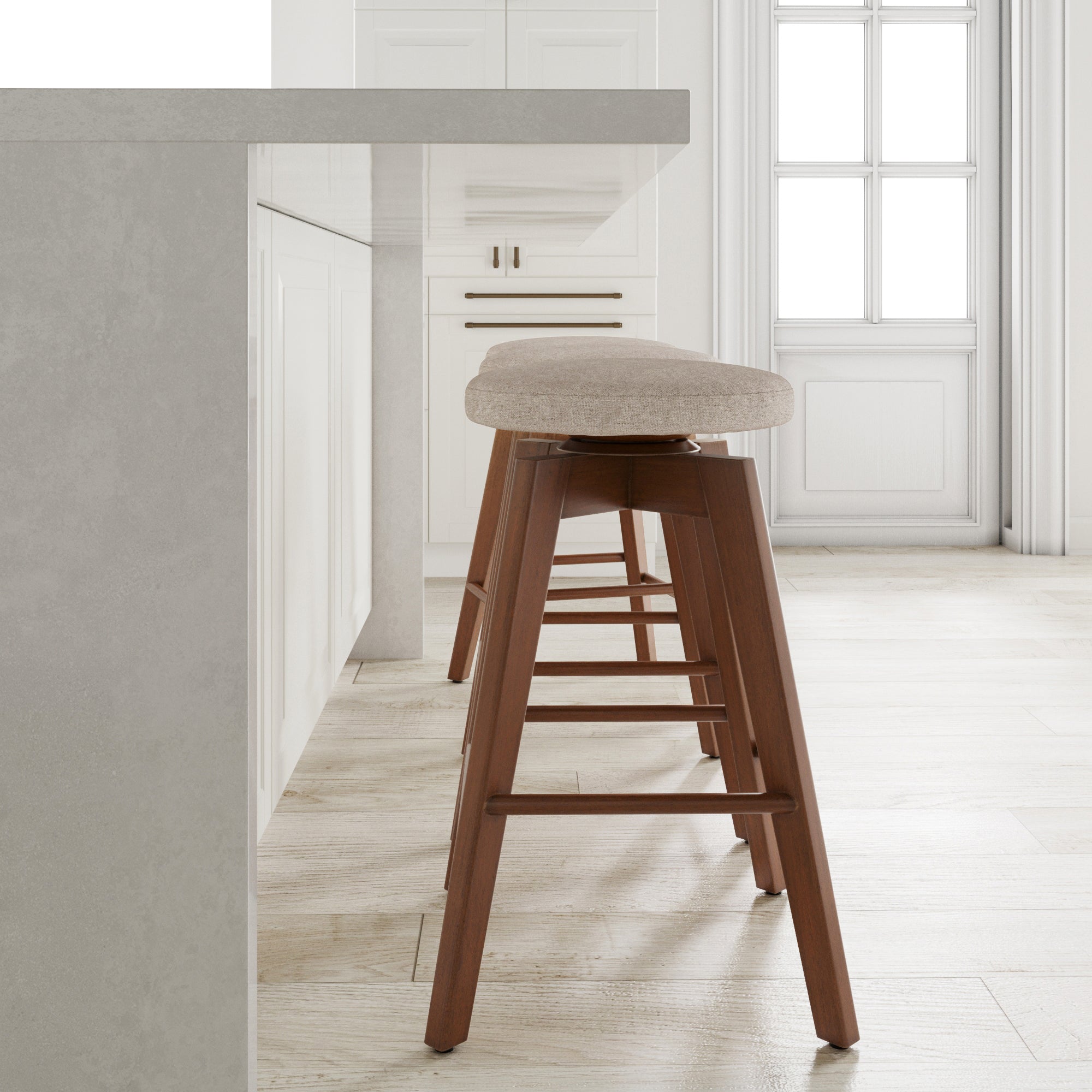 A modern kitchen with a light-colored countertop, white cabinetry, and a wooden barstool with a cushioned beige seat. Large windows in the background allow natural light into the bright, minimalist space.