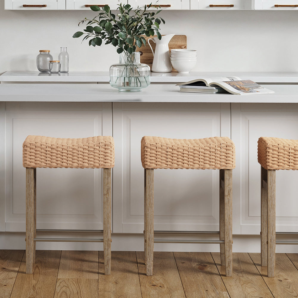 Three bar stools with woven tan seats and wooden legs positioned in front of a white kitchen island.