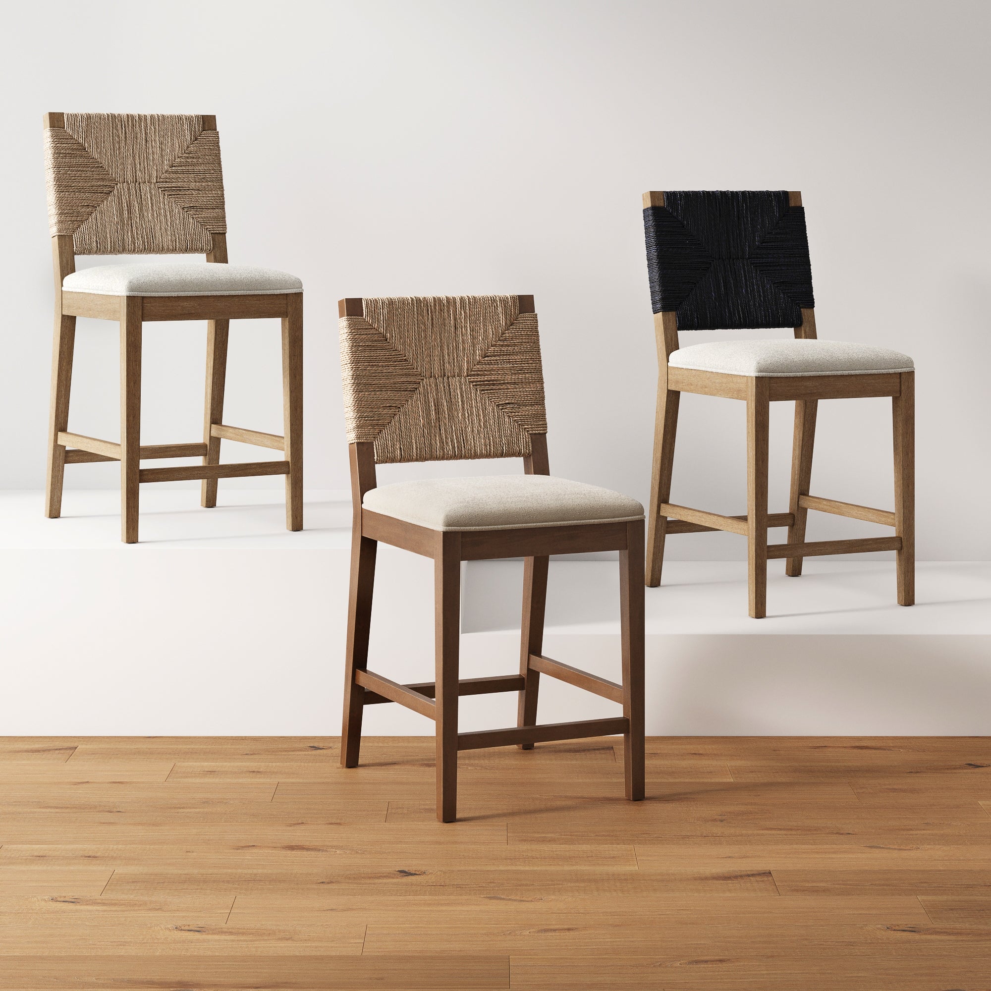 Three wooden chairs with beige upholstered seats and woven, geometric-patterned backrests—two in natural fiber and one in black—are arranged on a wooden floor against a plain, light-colored backdrop.