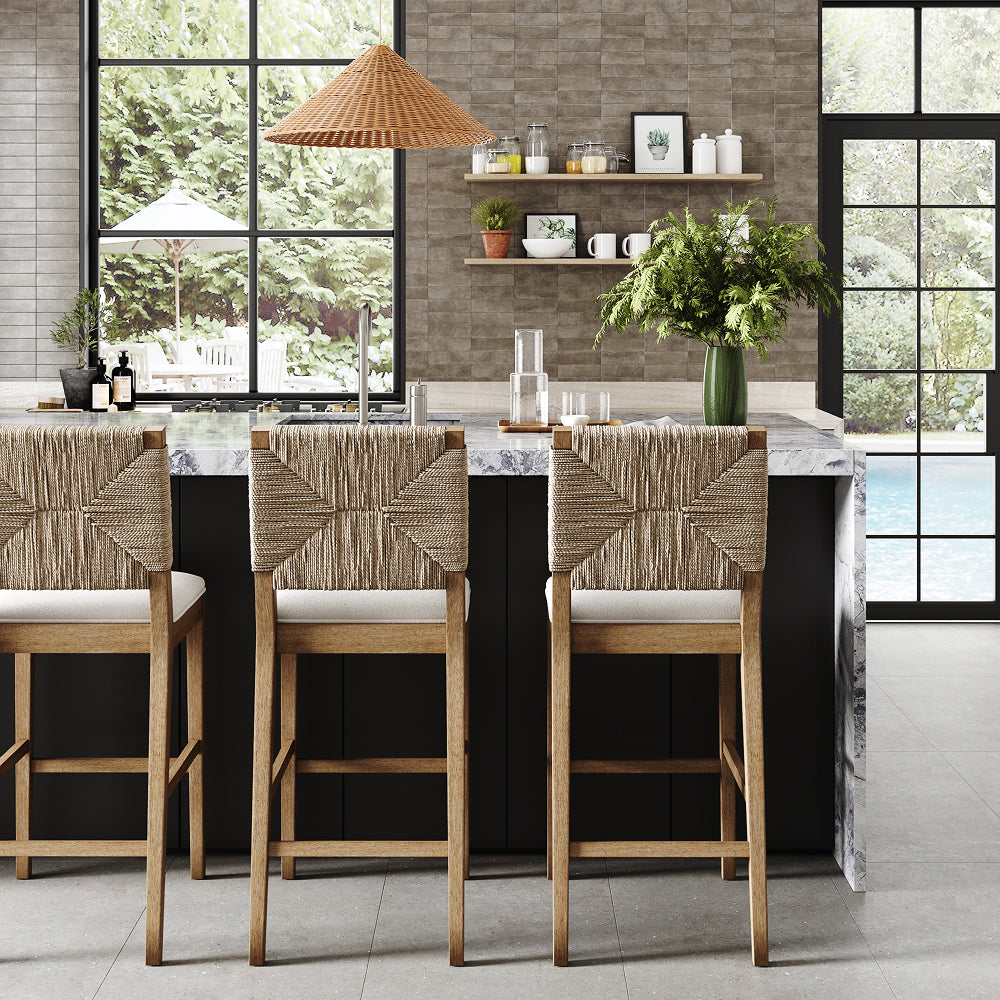Three wooden bar stools with woven backs face a marble-topped kitchen island with a sink and open shelving.