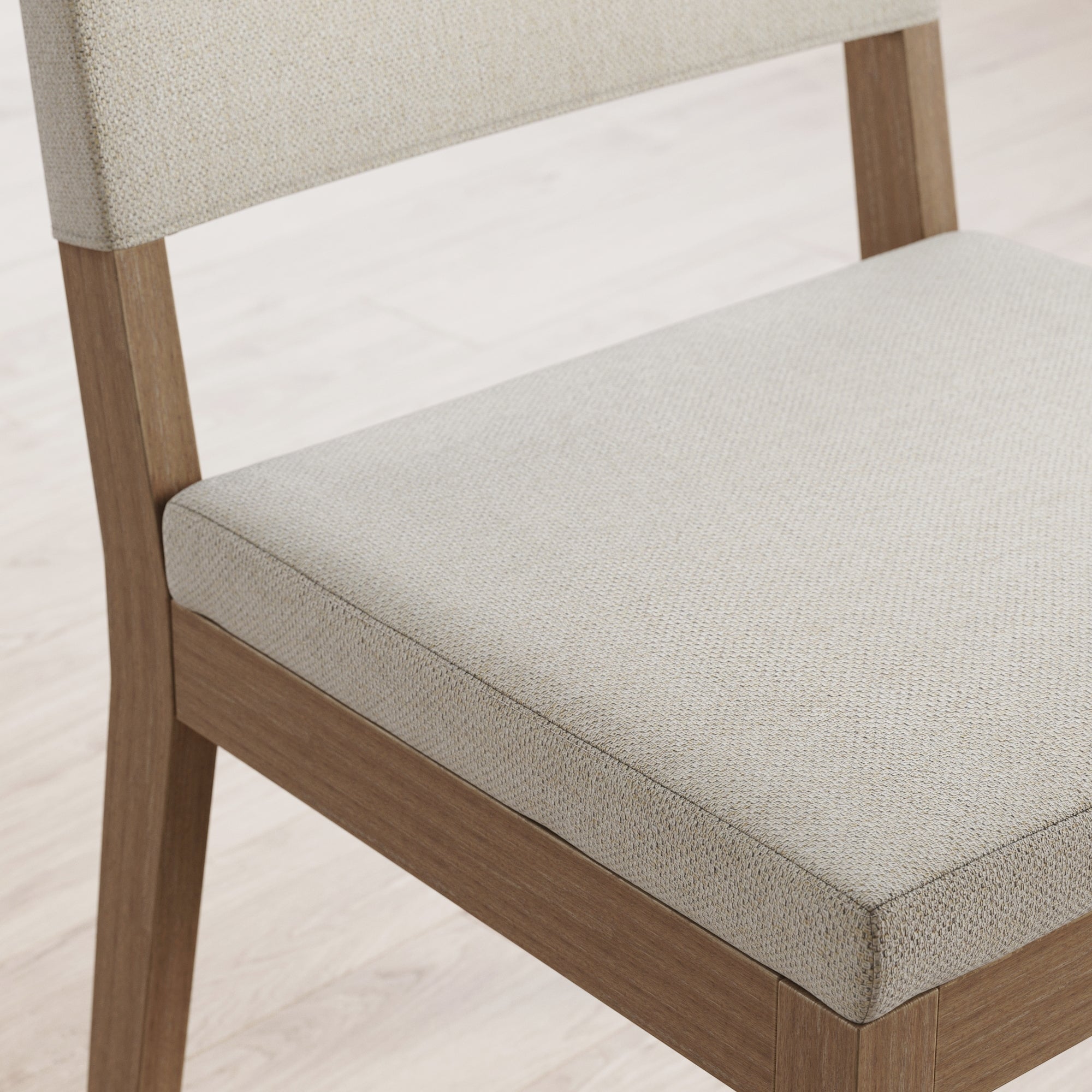 A wooden chair with light beige upholstered seat and backrest, placed on a light-colored hardwood floor.