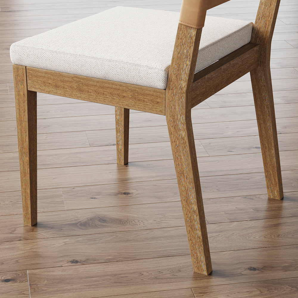 Wooden dining chair with a light-colored upholstered seat and tan leather detail on the backrest, set on a hardwood floor.