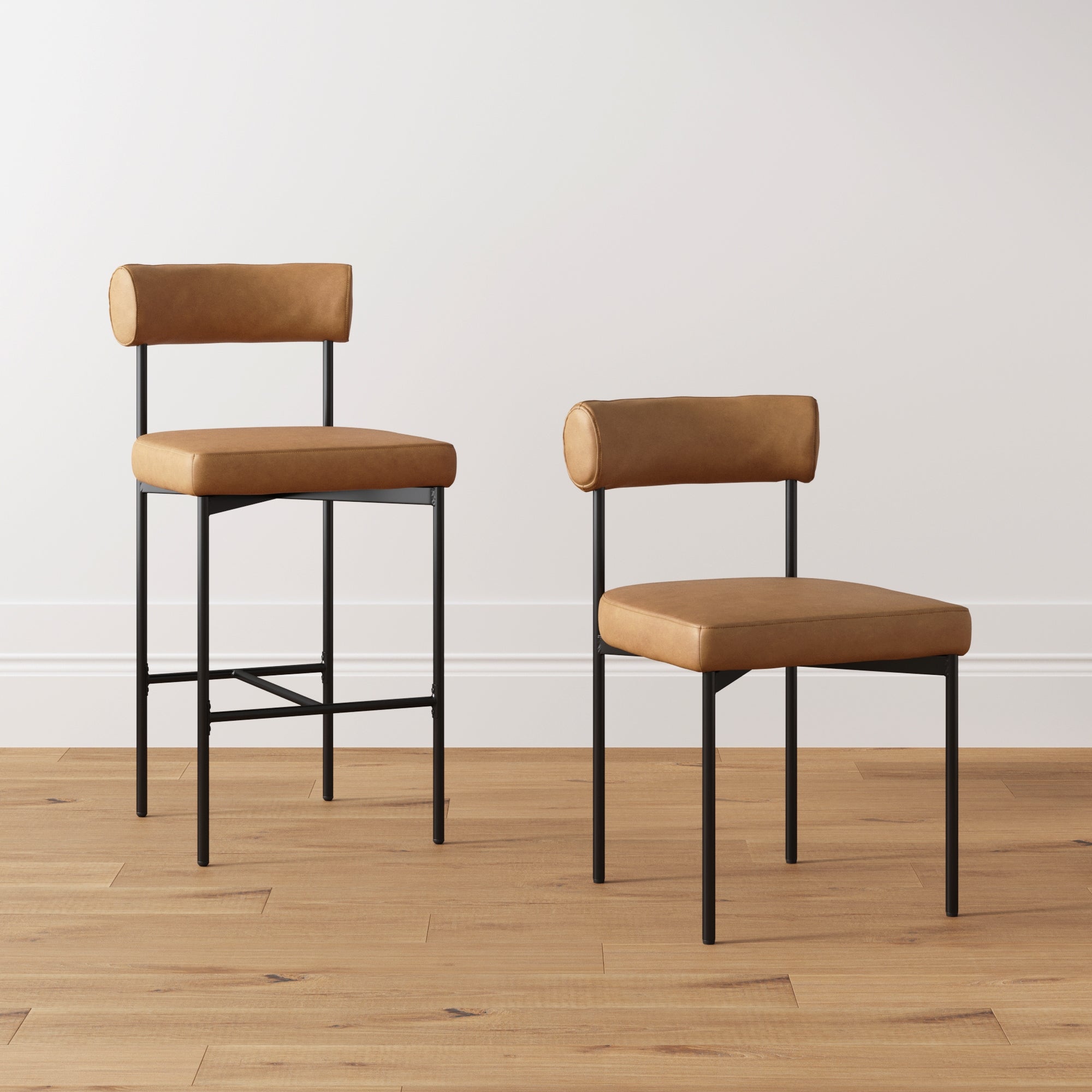 Two modern chairs with tan leather seats and backs, black metal legs, and simple minimalist design are placed on a light wood floor against a plain white wall. One chair has longer legs than the other.