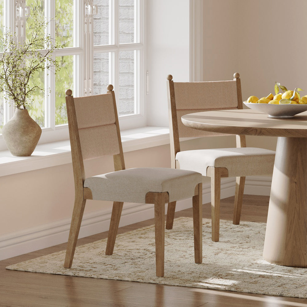 Two upholstered dining chairs with wooden frames placed around a round wooden table topped with a bowl of lemons.