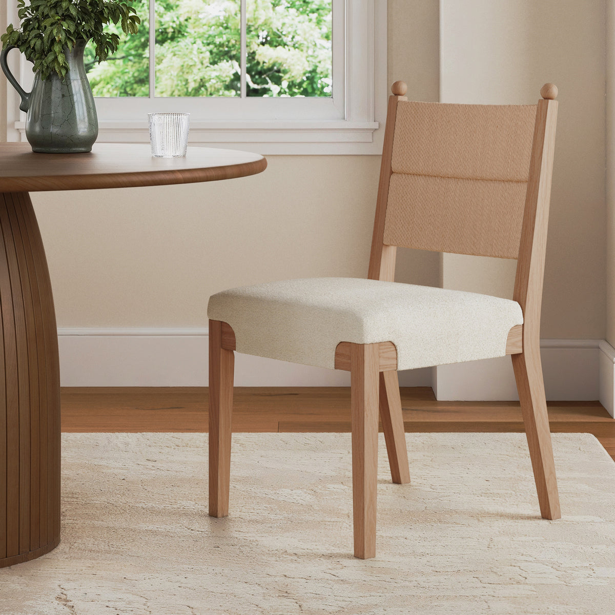 A light wood dining chair with a woven backrest and upholstered seat positioned next to a round wooden table.