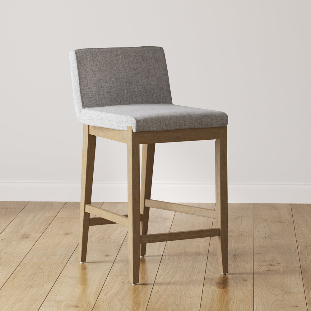 Counter stool with a light gray upholstered seat and back on a light wood frame.