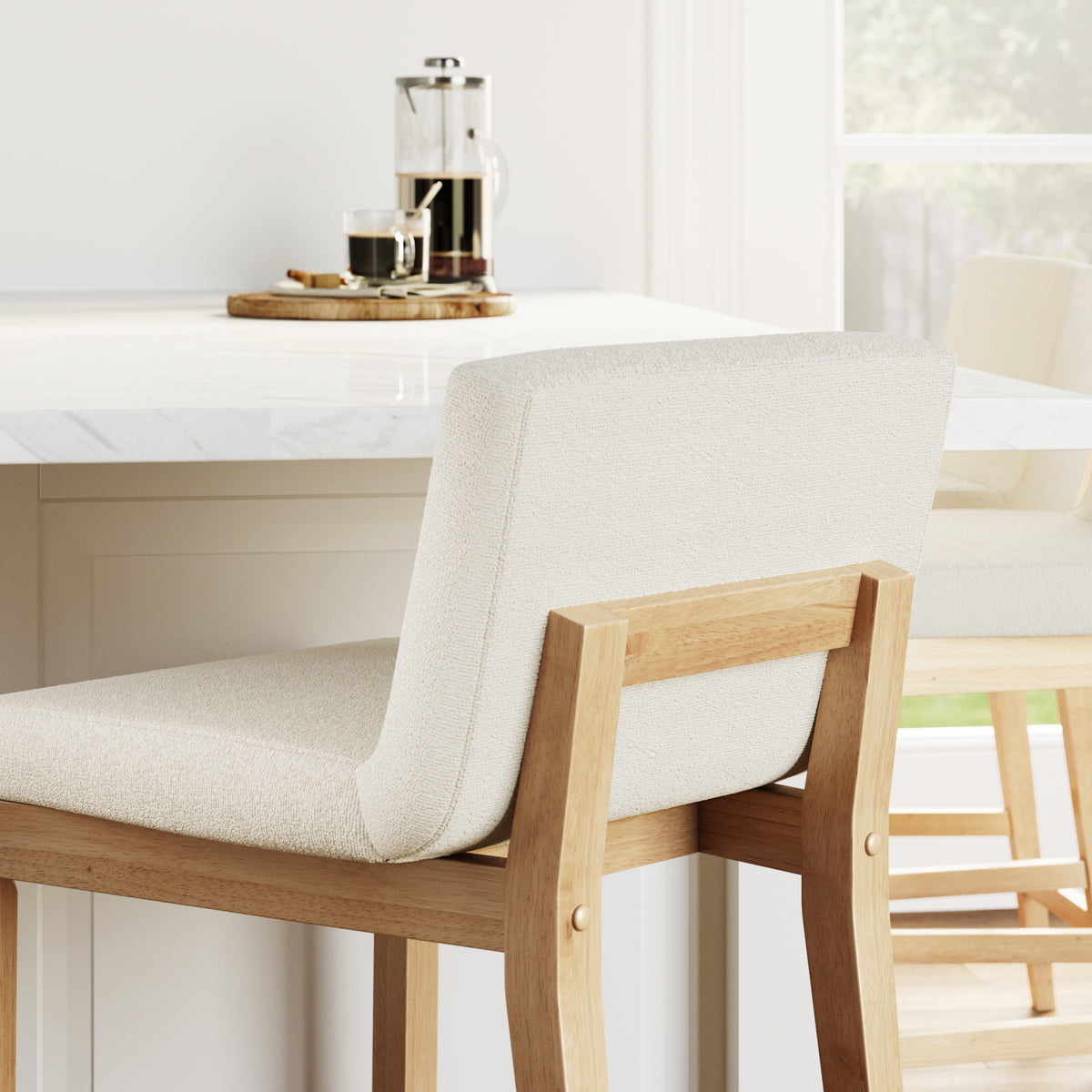Two upholstered wooden bar stools sit at a marble kitchen island with a coffee press and cup in the background.