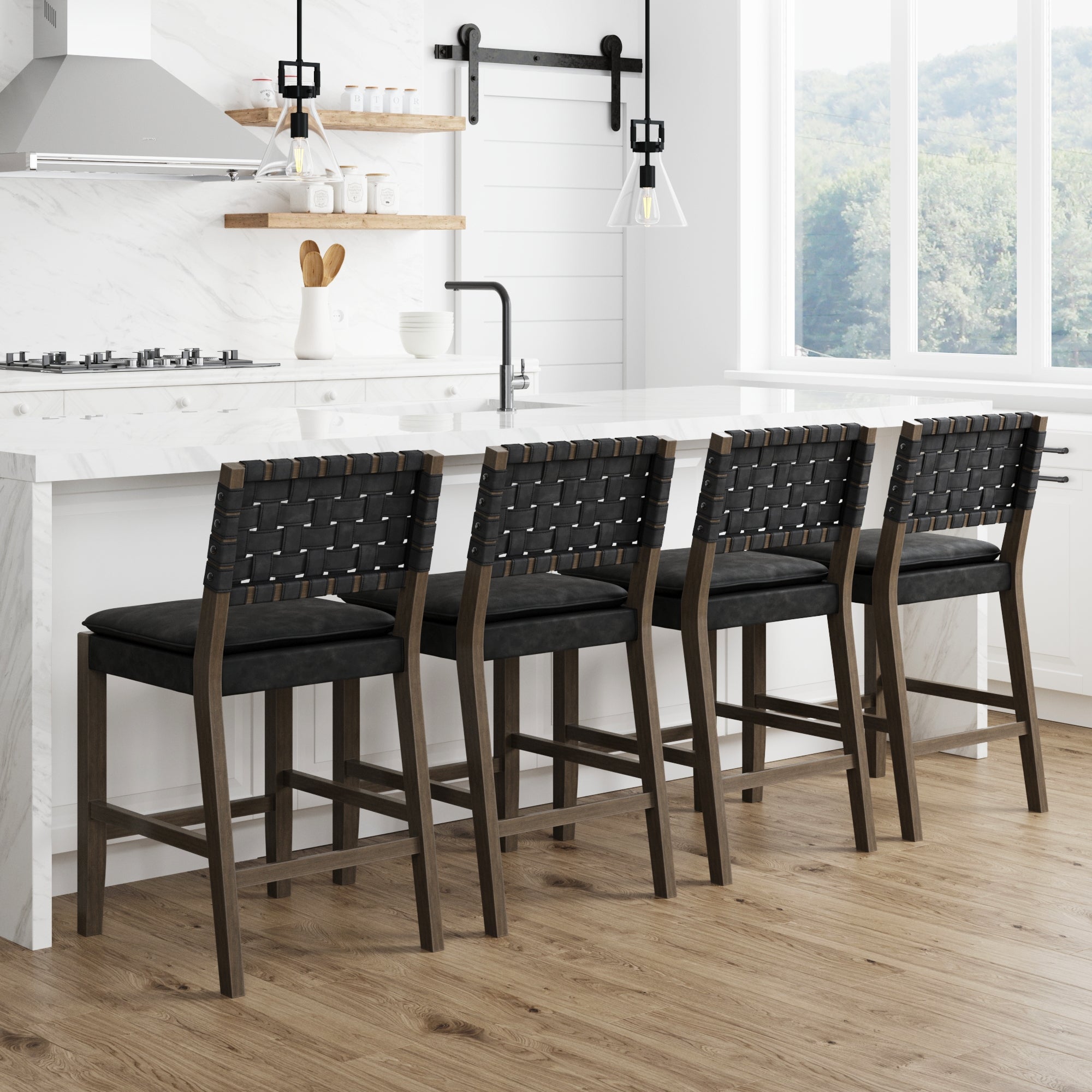 Four woven-back bar stools with dark wooden frames and black seats are lined up along a white marble kitchen island in a bright, modern kitchen with wood flooring and large windows.