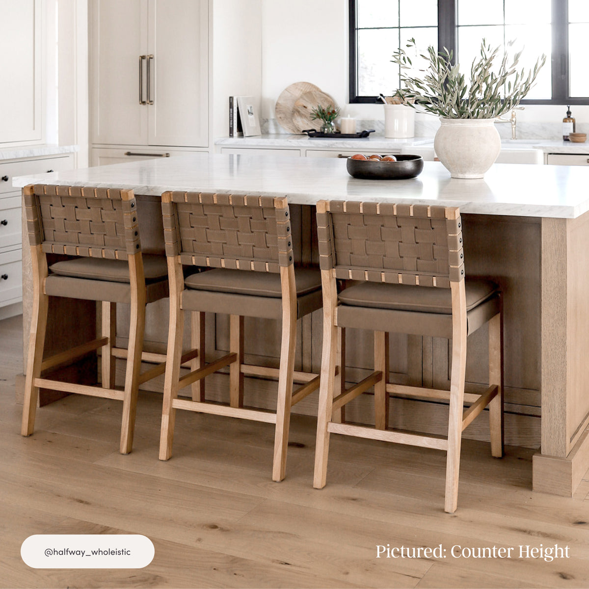 Three Nathan James Faux Suede Woven Bar Stool Brown 29″ bar stools with solid wood frames, faux suede seats, and woven backrests pulled up to a kitchen island.