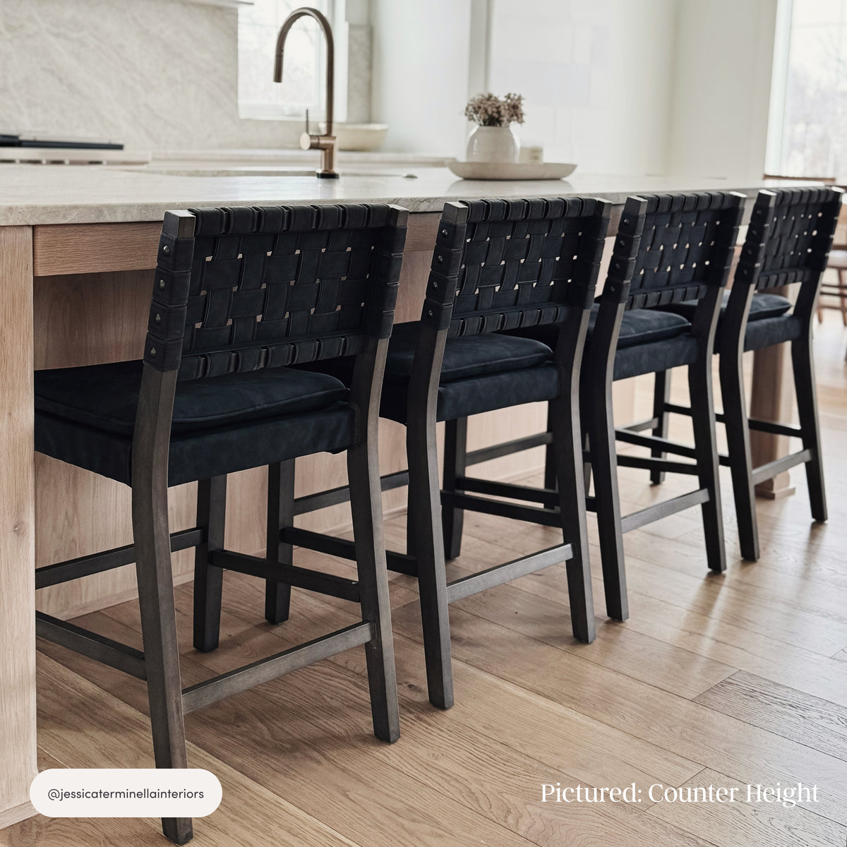 Four Nathan James Faux Suede Woven Bar Stools Black with woven backs and padded seats positioned at a kitchen island.