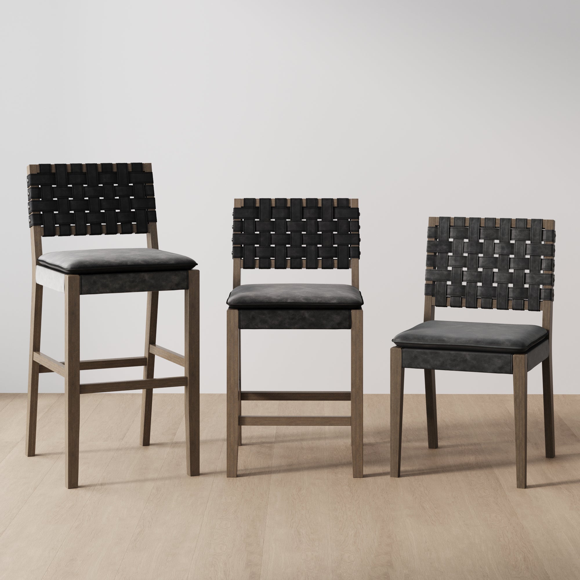 Three wooden chairs with black woven leather backs and cushioned seats are arranged side by side on a light wood floor against a plain light-colored wall. The chairs vary in height.