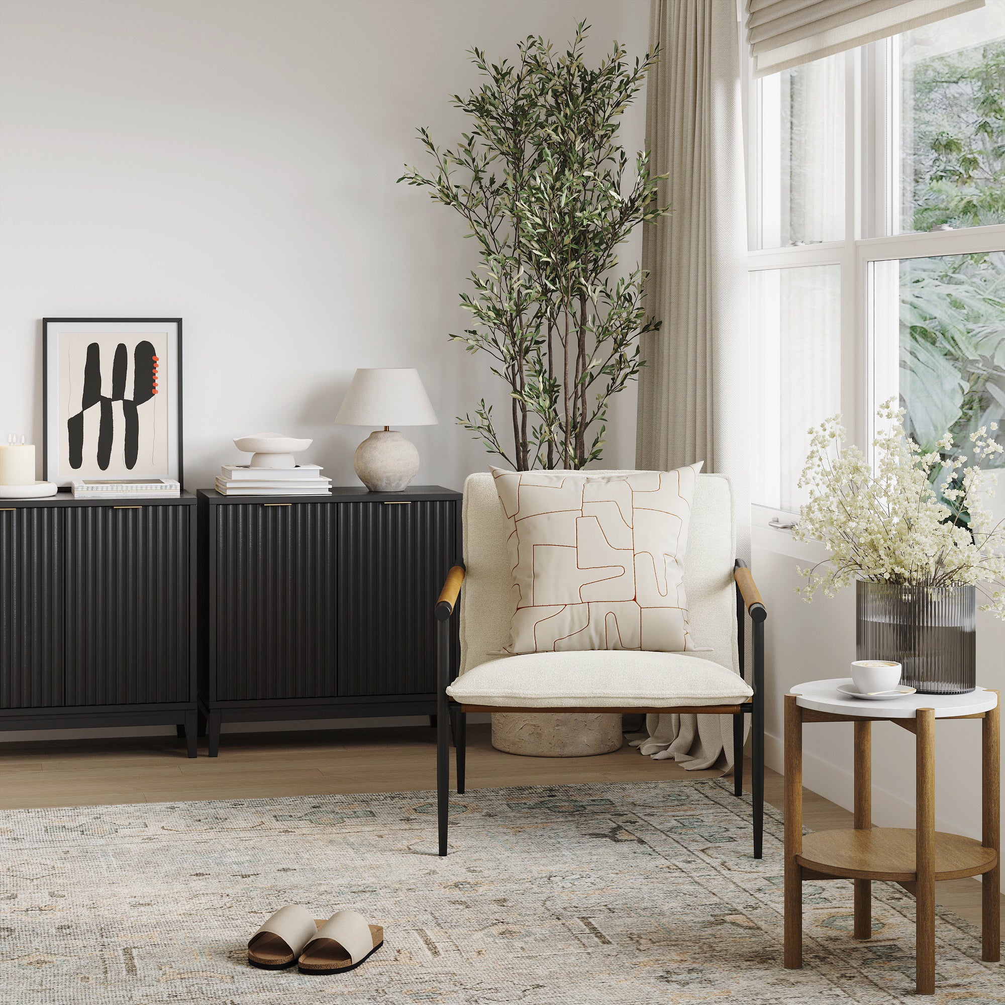A modern living room with a cream armchair, geometric cushion, small side table with flowers, black cabinets, framed art, white lamp, potted plant, and sunlight streaming through large windows. Slippers are on a patterned rug.