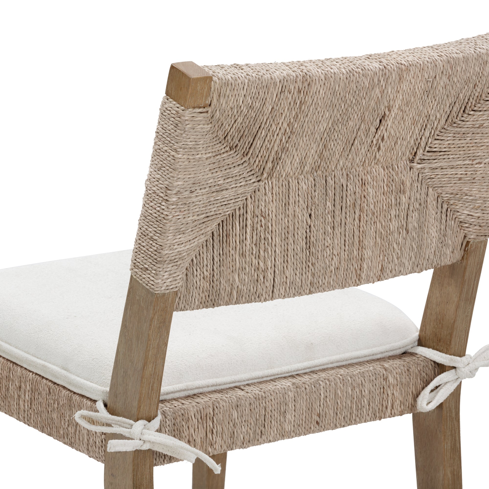 A close-up of a chair with a natural wood frame, a woven rope backrest and seat, and a white cushioned seat tied to the frame with white fabric strings.