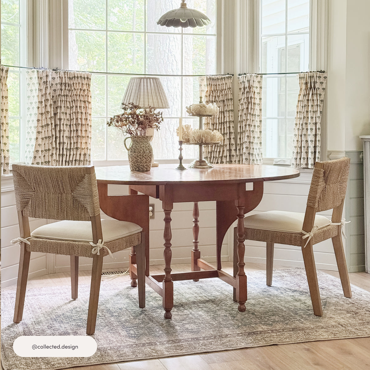 Two Nathan James Boucle & Seagrass Dining Chair Light Brown chairs with seagrass backrests and light-colored upholstered seats positioned at a wooden drop-leaf table in front of a window.