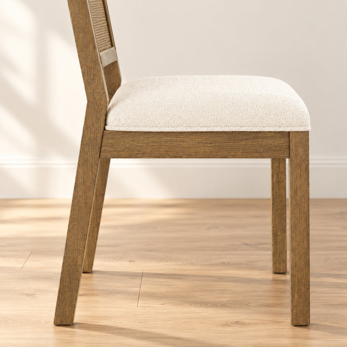 Side view of a wooden dining chair with a cane backrest and an off-white upholstered seat.