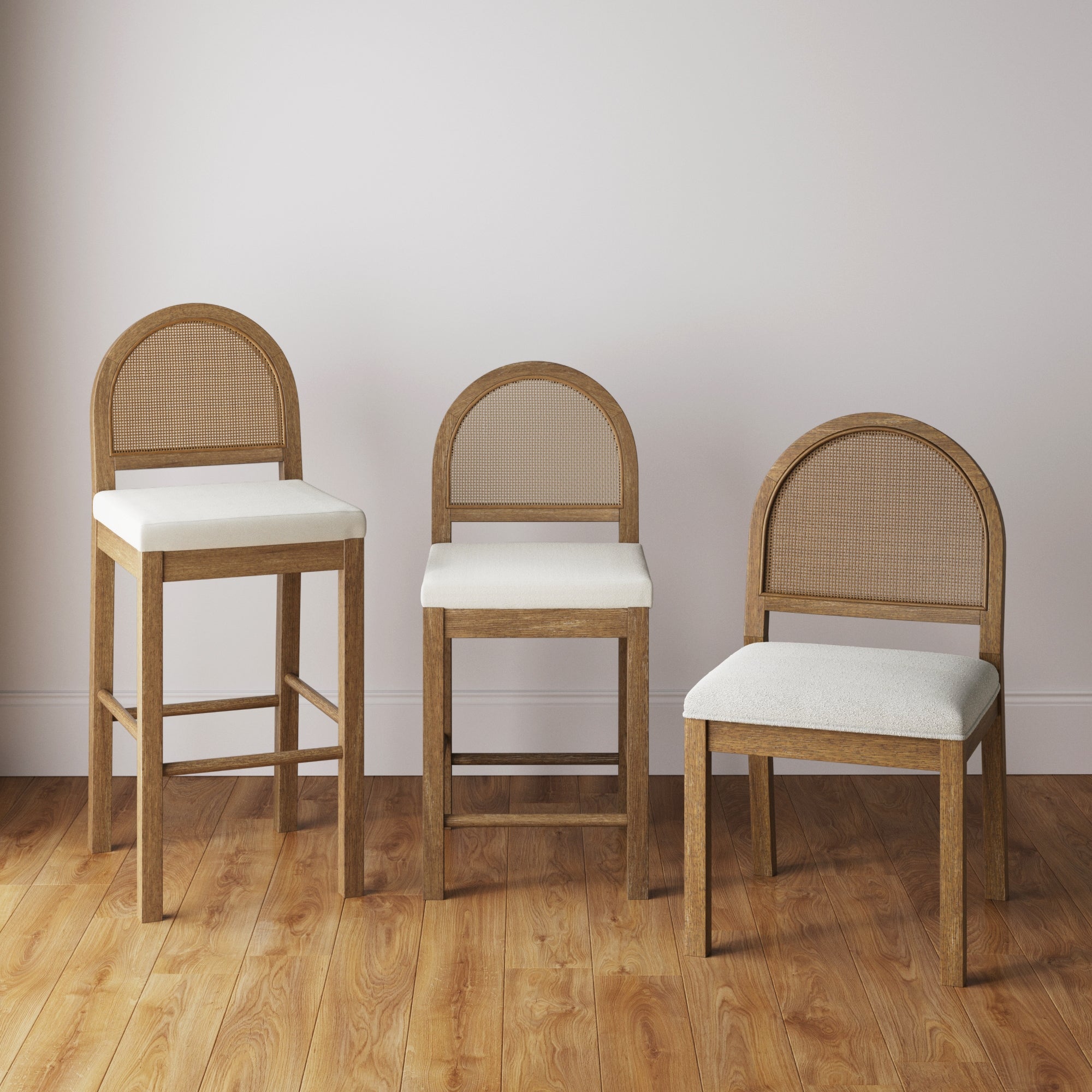 Three wooden chairs with rounded backs and light-colored cushioned seats are arranged side by side on a hardwood floor against a plain white wall. Each chair is a different height.