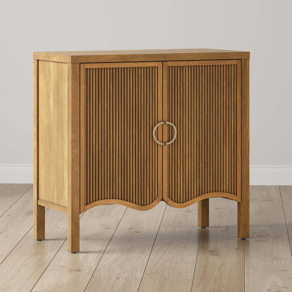 Light wood cabinet with two fluted doors and circular gold hardware on four legs.