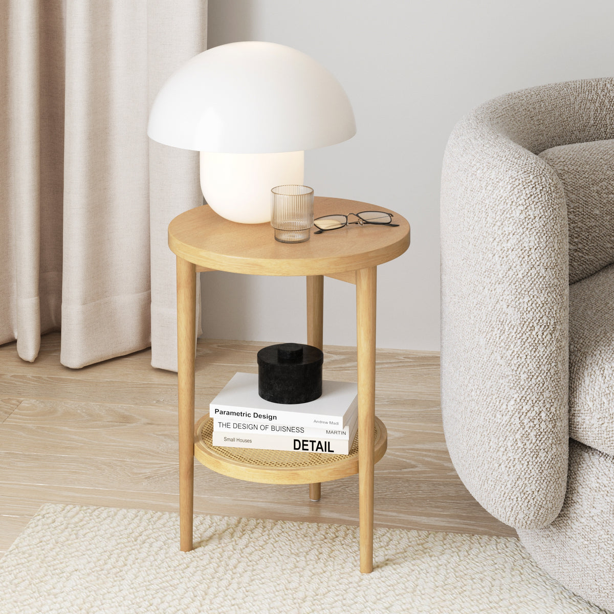 A small round wooden side table with a white mushroom-shaped lamp, a pair of eyeglasses, and a glass of water on top. The lower shelf holds stacked books and a black box, next to a beige textured sofa.