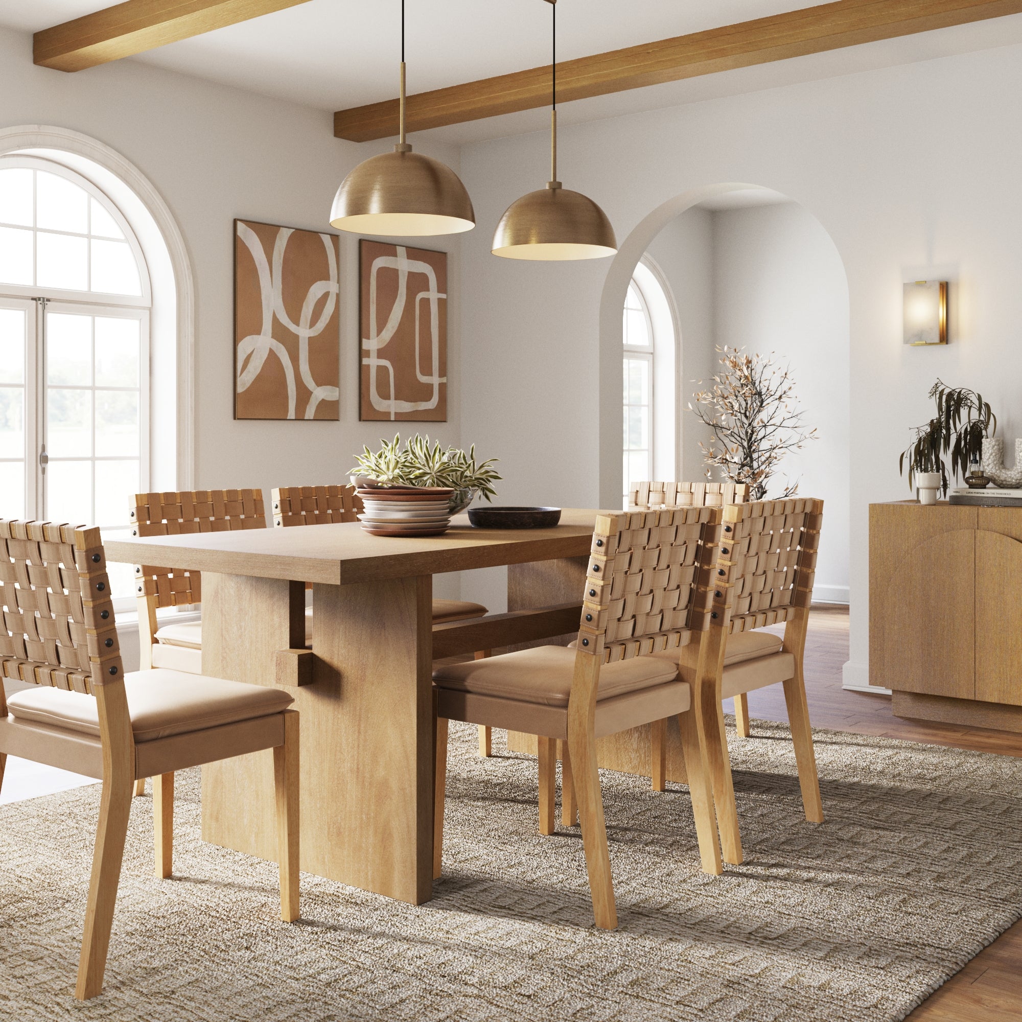 A modern dining room with a wooden table, six woven-back chairs, pendant lights, abstract wall art, a sideboard, and large arched windows letting in natural light. A neutral rug covers the wooden floor.