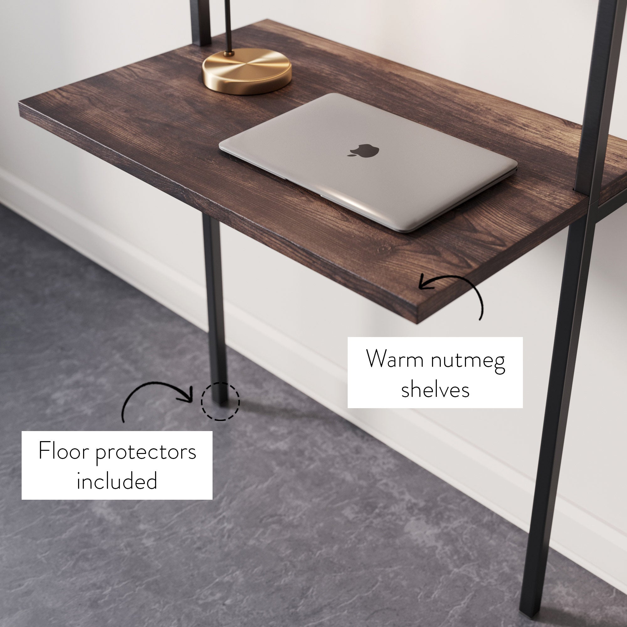 A desk with warm nutmeg-colored shelves holds a closed silver laptop. A gold lamp is in the background, and a label notes that floor protectors are included. The floor is a dark gray tile.
