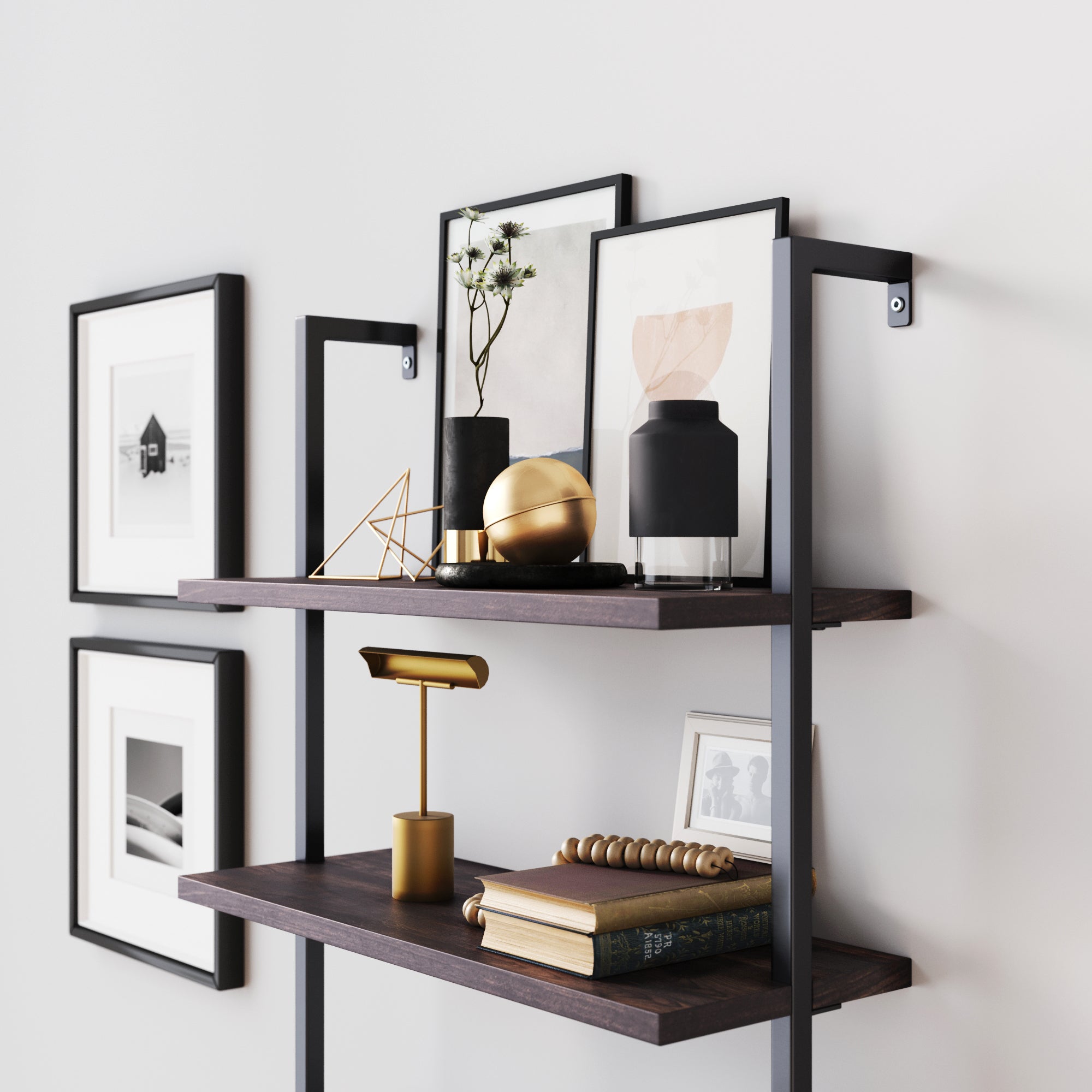 A modern wall-mounted shelving unit displays books, decorative objects, framed art, a gold desk lamp, and a black vase with small flowers against a white wall with additional black-and-white framed photographs.