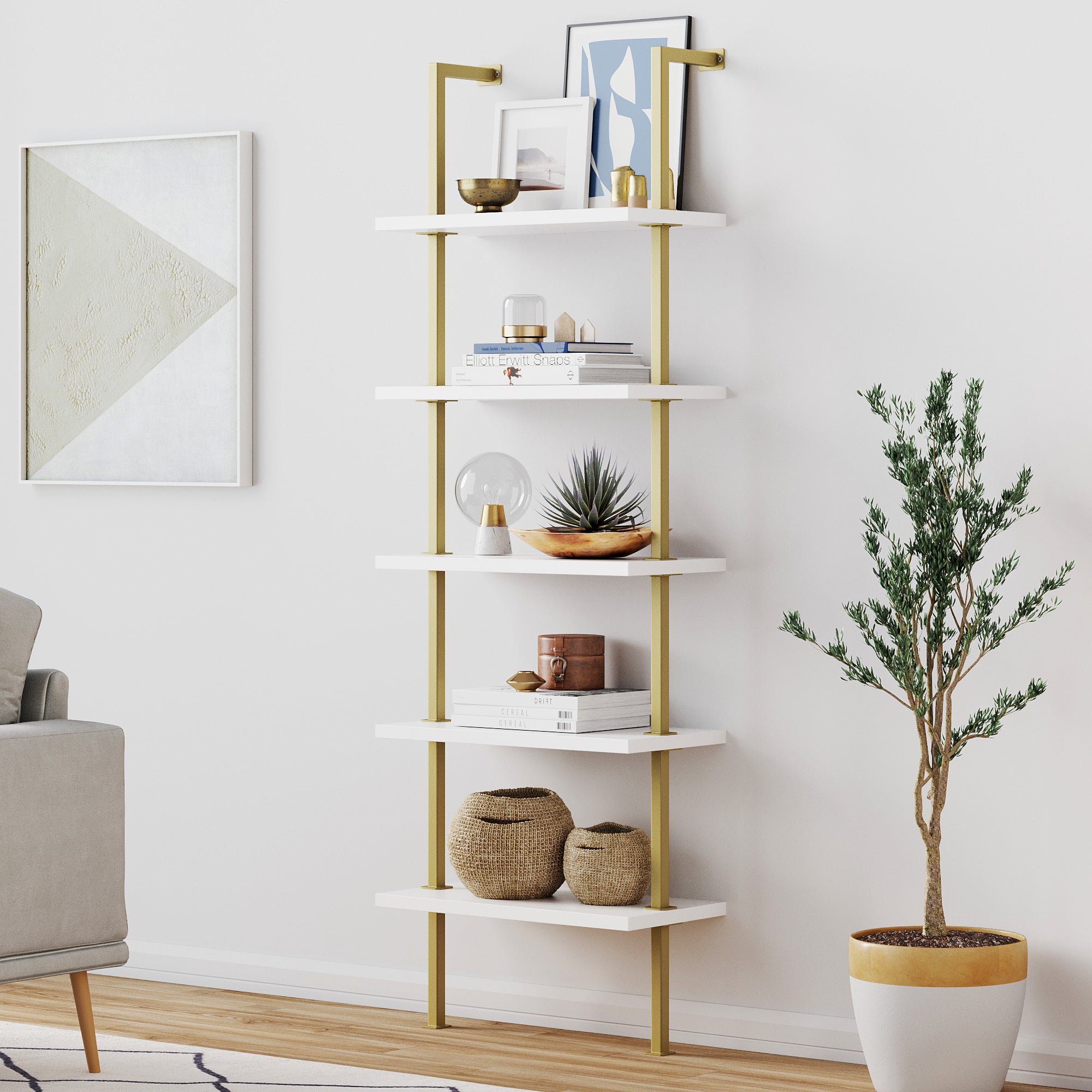 A modern white and gold shelving unit with decor items, books, baskets, and plants stands against a white wall next to a potted plant. A framed abstract art piece hangs on the left wall.