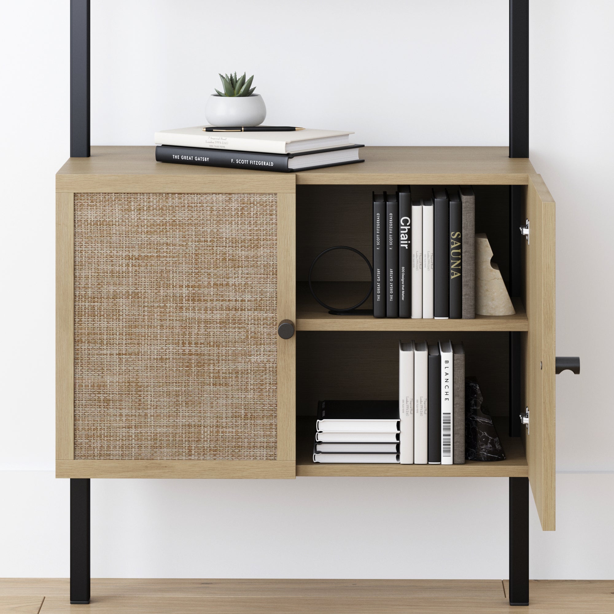 A wooden cabinet with a woven door panel, partially open to reveal shelves holding neatly stacked books. On top, there are more books and a small potted succulent. The cabinet stands on black metal legs.