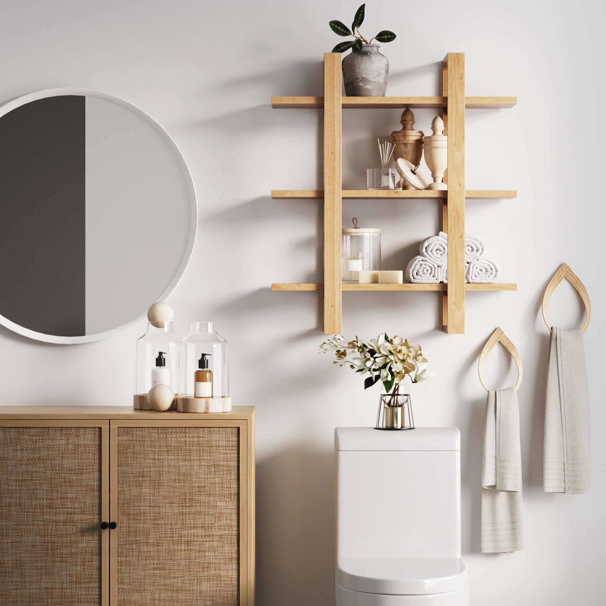 Modern bathroom with a round mirror, wooden shelves holding decor and rolled towels, a cabinet with toiletries, a vase with flowers on the toilet tank, and two towels hanging on wall hooks.