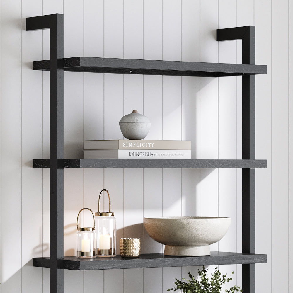A black metal and wood three-tier wall shelf holding two books, a small ceramic jar, two glass lanterns, a decorative bowl, and a small potted plant.