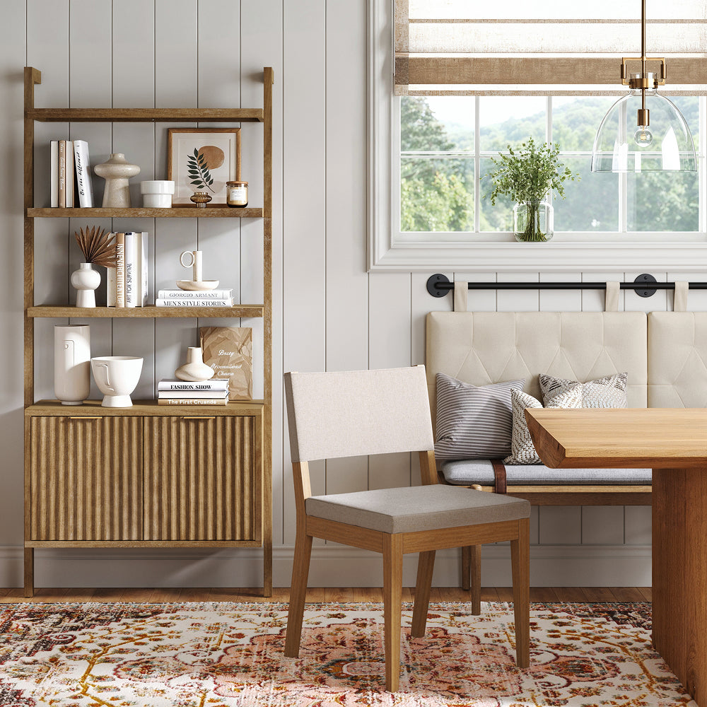 A wooden dining room featuring a tall shelving unit filled with decor, a cushioned chair, and a built-in bench seat next to a window.