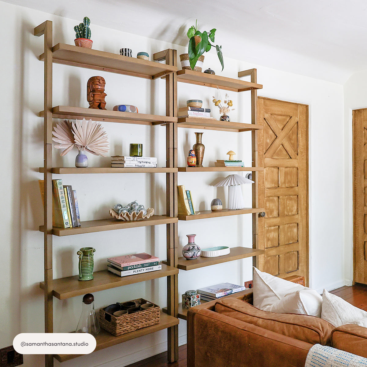 Two Nathan James Modern 6-Shelf Wall Mounted Solid Wood Bookcase Light Brown (Set of 4) units mounted side-by-side on a white wall, filled with books, small decorative objects, and indoor plants.