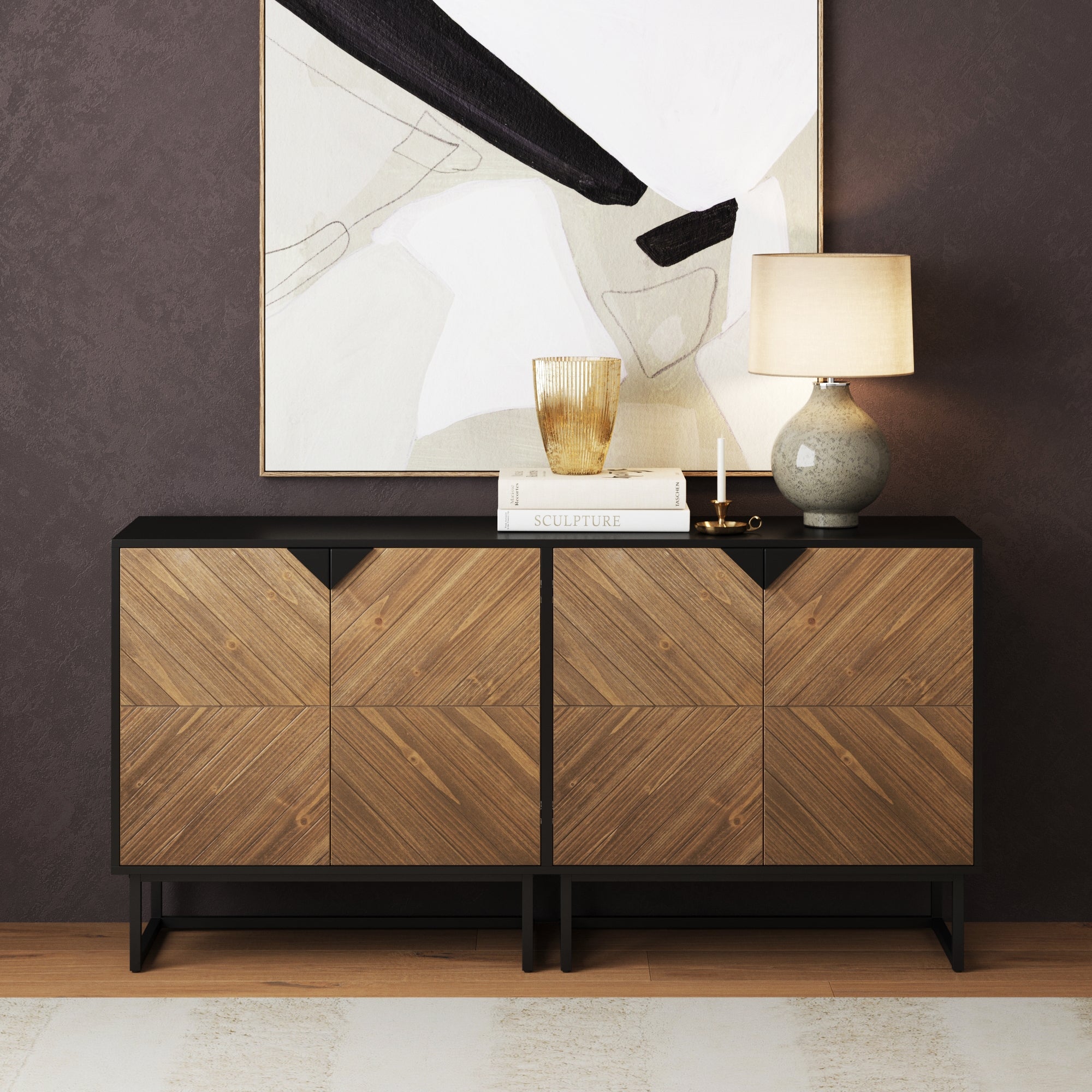 A modern sideboard with geometric wooden doors sits against a dark wall. On top are a lamp, a glass, a book, and candles. An abstract art piece hangs above it. The floor is light wood with a rug.