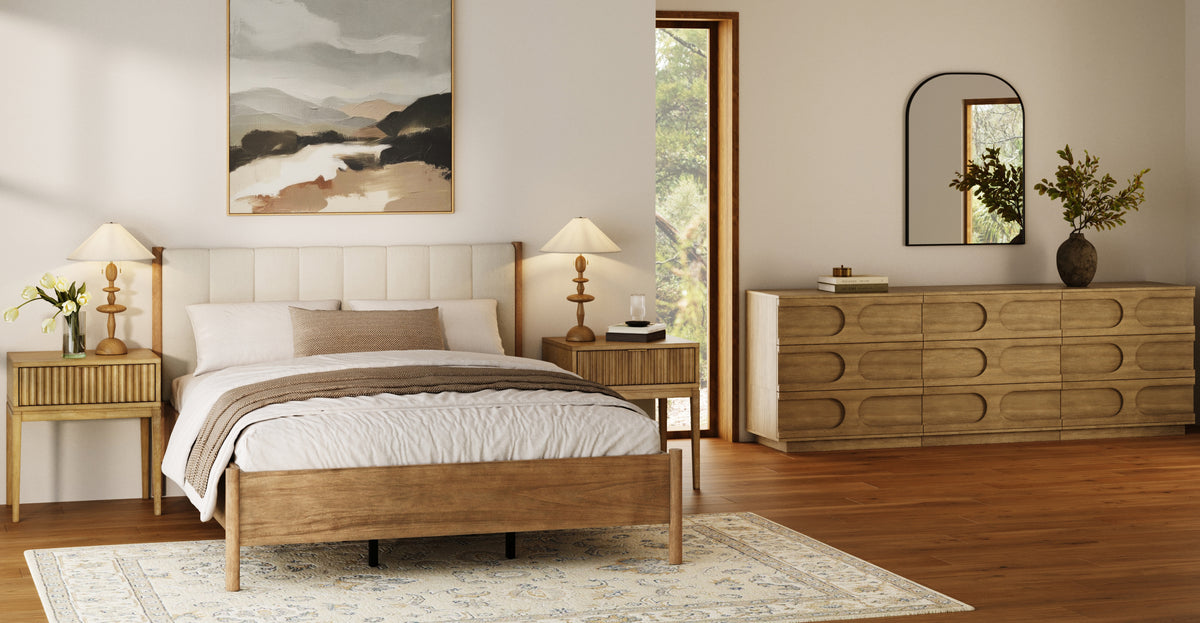 A bedroom featuring a wooden bed frame with a tufted headboard, two matching nightstands with lamps, and a long wooden dresser topped with a vase and mirror.