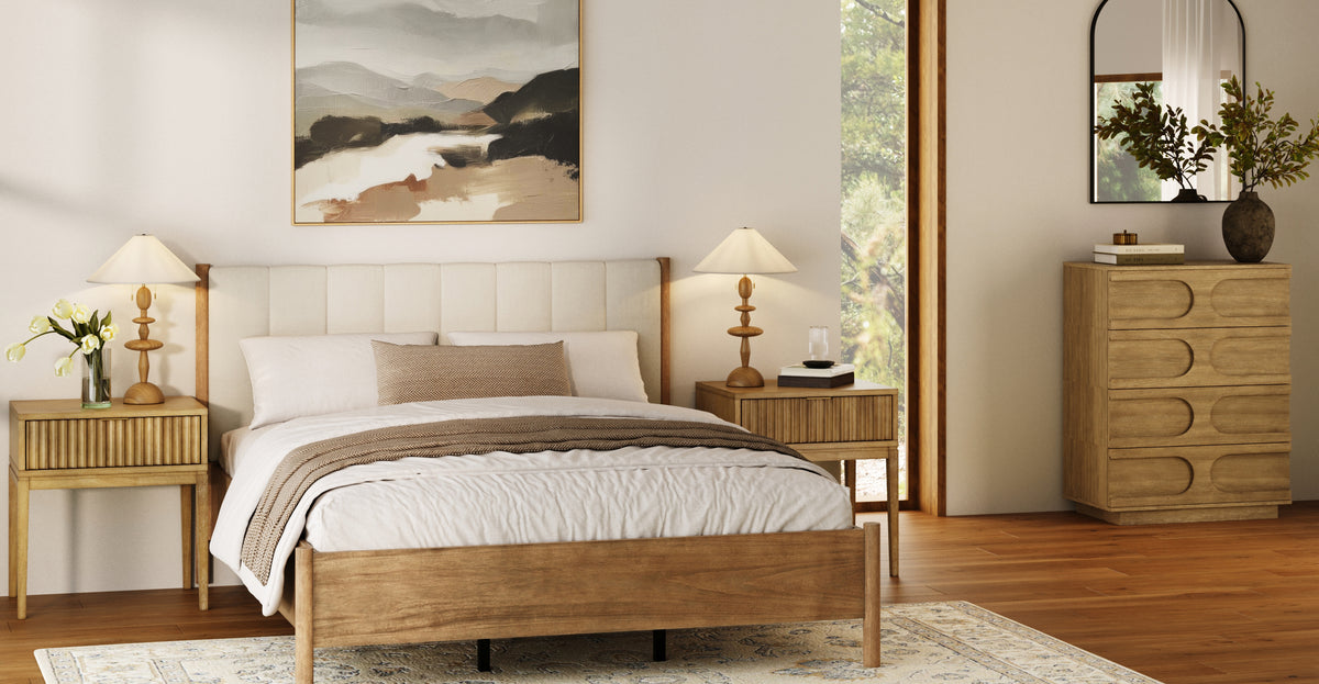 A bedroom featuring a wooden bed frame, two nightstands with lamps, and a wooden dresser with a mirror, all set against a neutral wall with an abstract landscape painting.