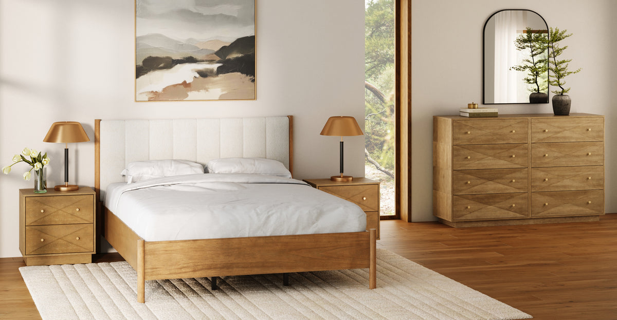 A bedroom featuring a wooden bed frame with a white upholstered headboard, two matching wooden nightstands with brass lamps, and a wooden dresser topped with a mirror and a small plant.