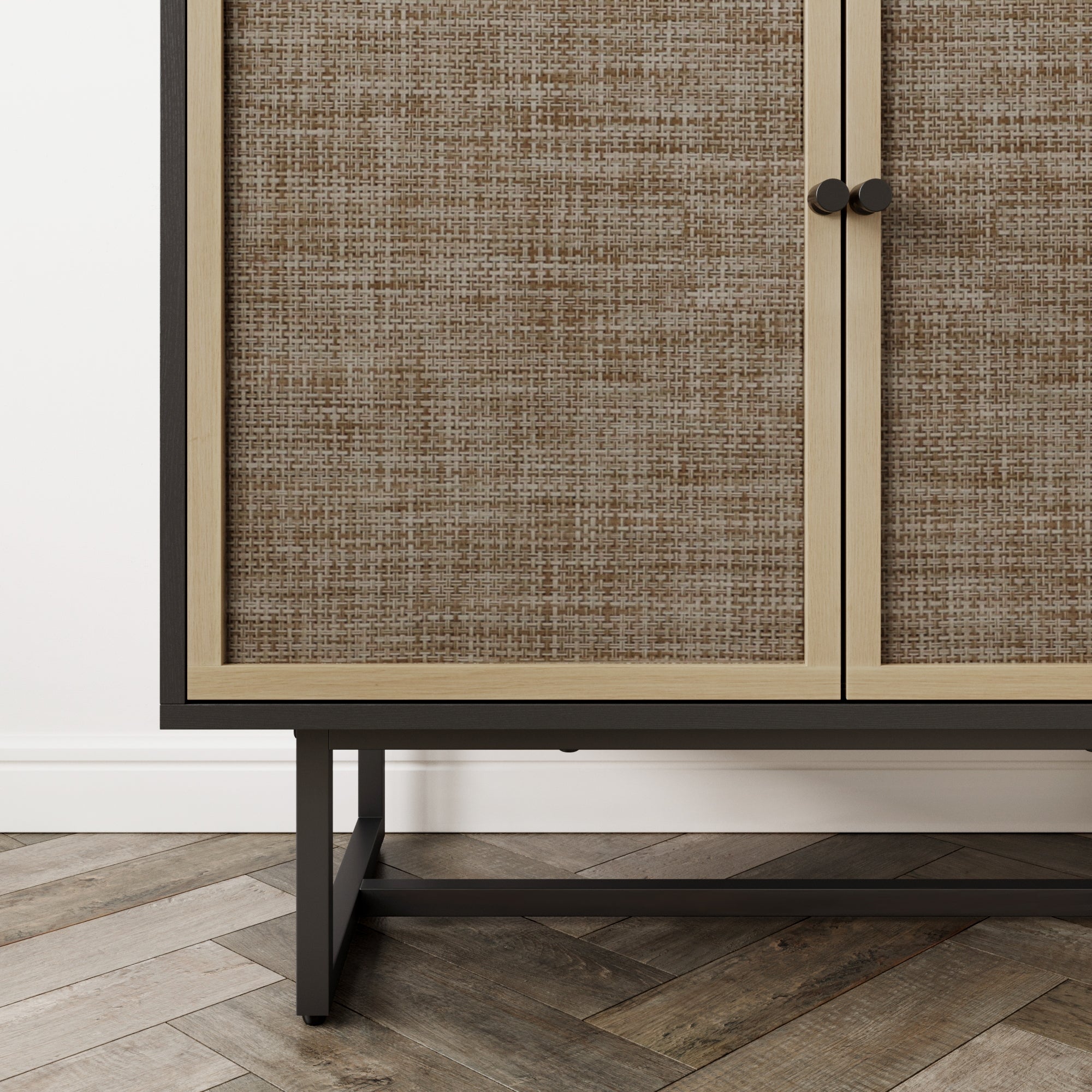 Close-up of a cabinet with textured, woven-patterned doors, black metal legs, and a chevron-patterned wooden floor beneath. The cabinet has a light wood frame and two round black handles.