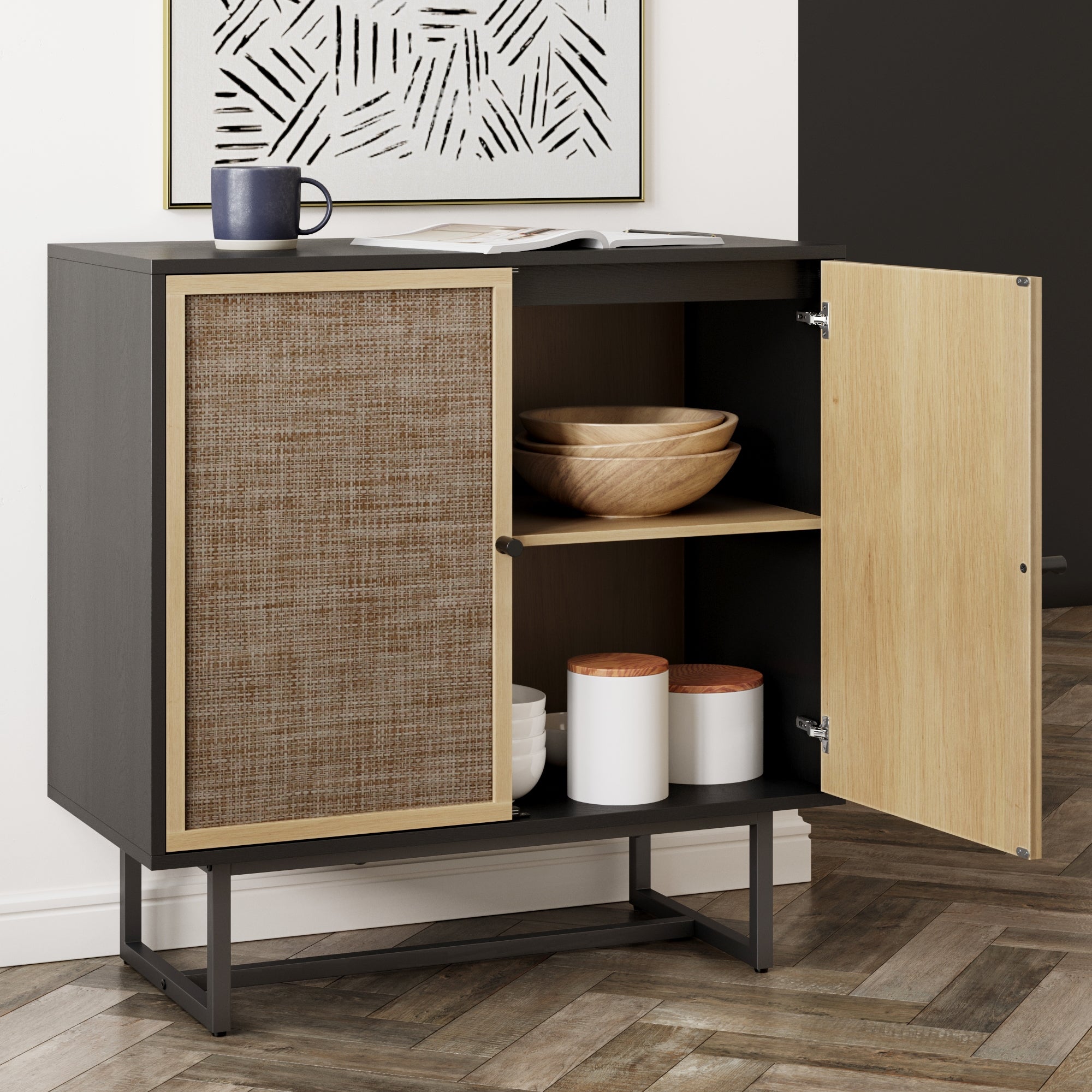 A modern cabinet with one door open, displaying wooden bowls and white containers on shelves. A cup and an open magazine rest on top. The cabinet has a woven panel and sits on a wooden floor.