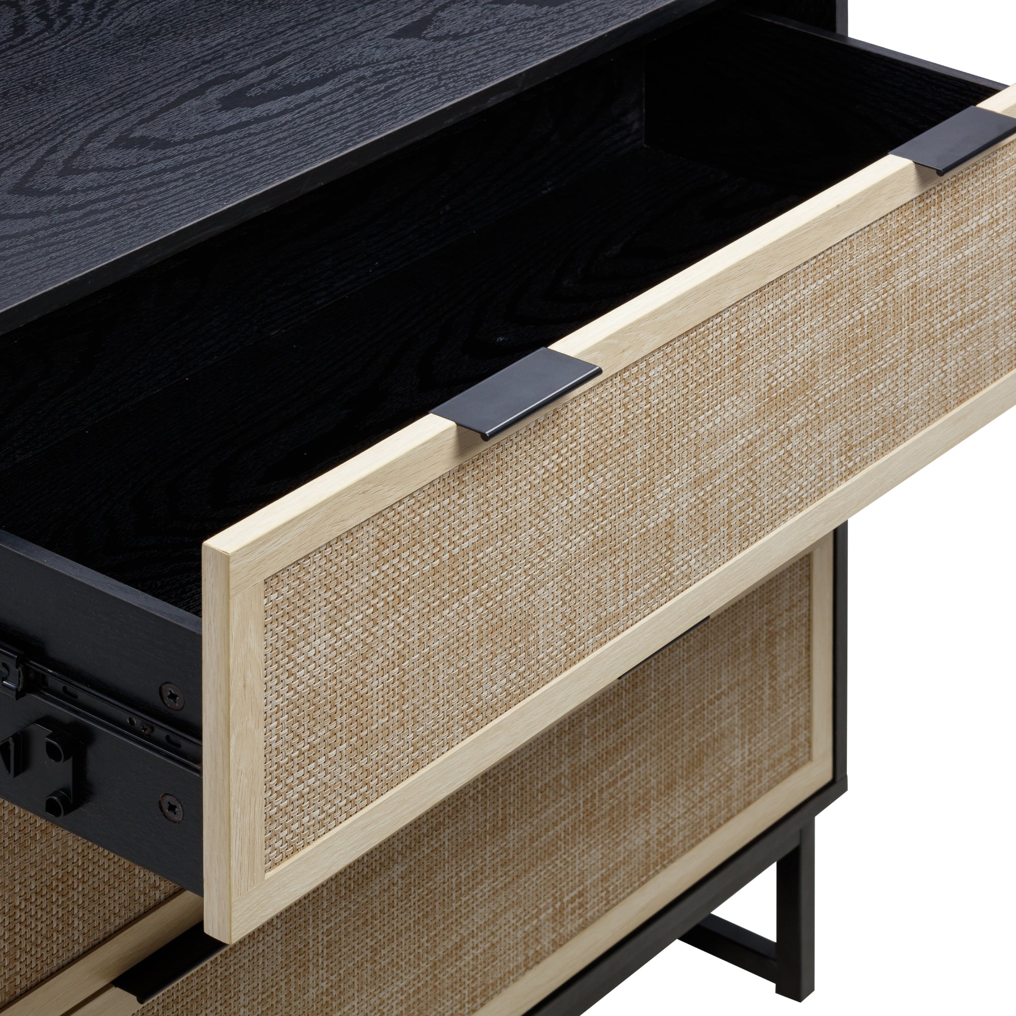 A close-up of a wooden dresser with a partially open drawer. The drawer front features a woven rattan design framed by light wood and is accented with black metal handles. The interior of the drawer is black.