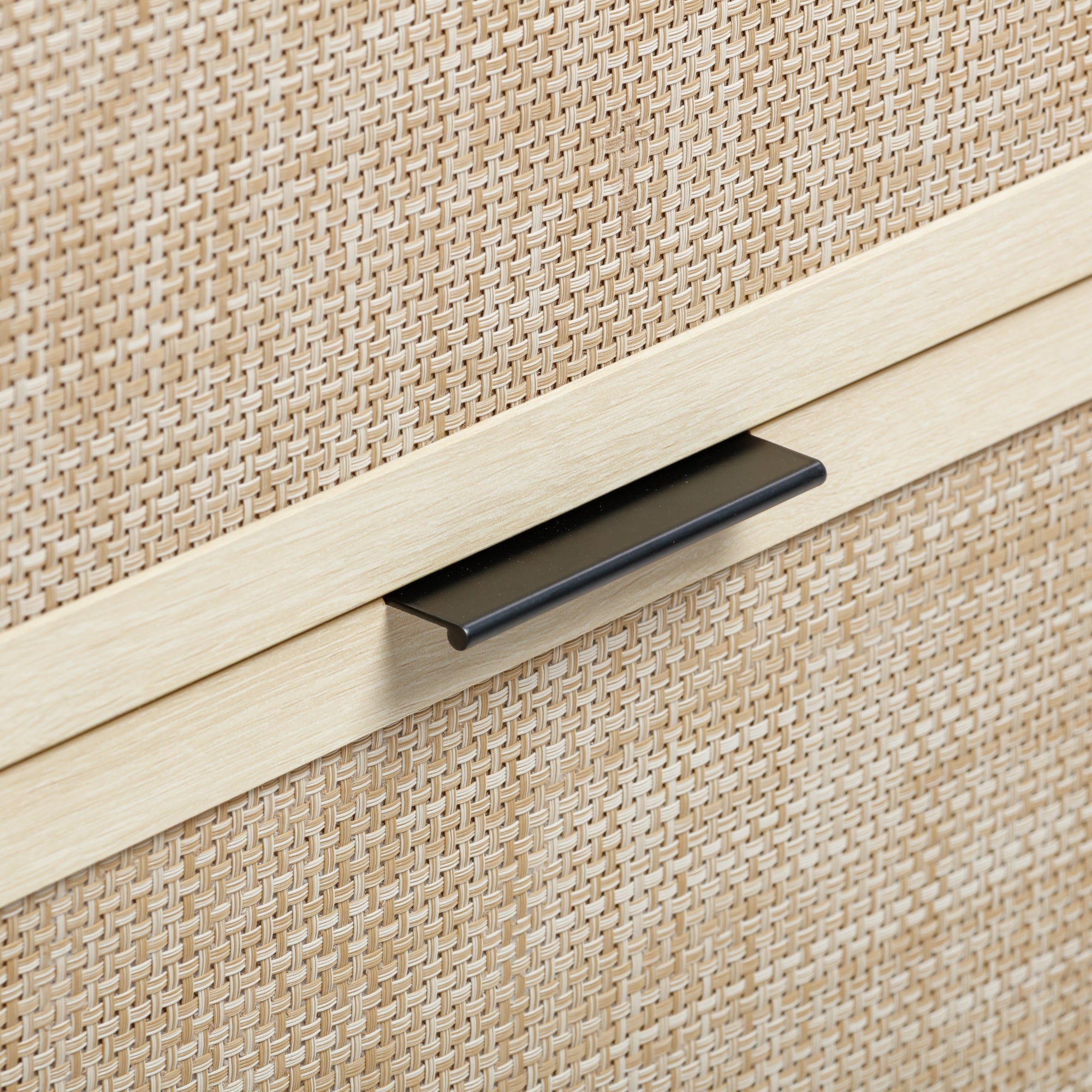 Close-up of a light-colored woven wicker cabinet with a sleek, rectangular black metal handle. The texture and pattern of the wicker are clearly visible.