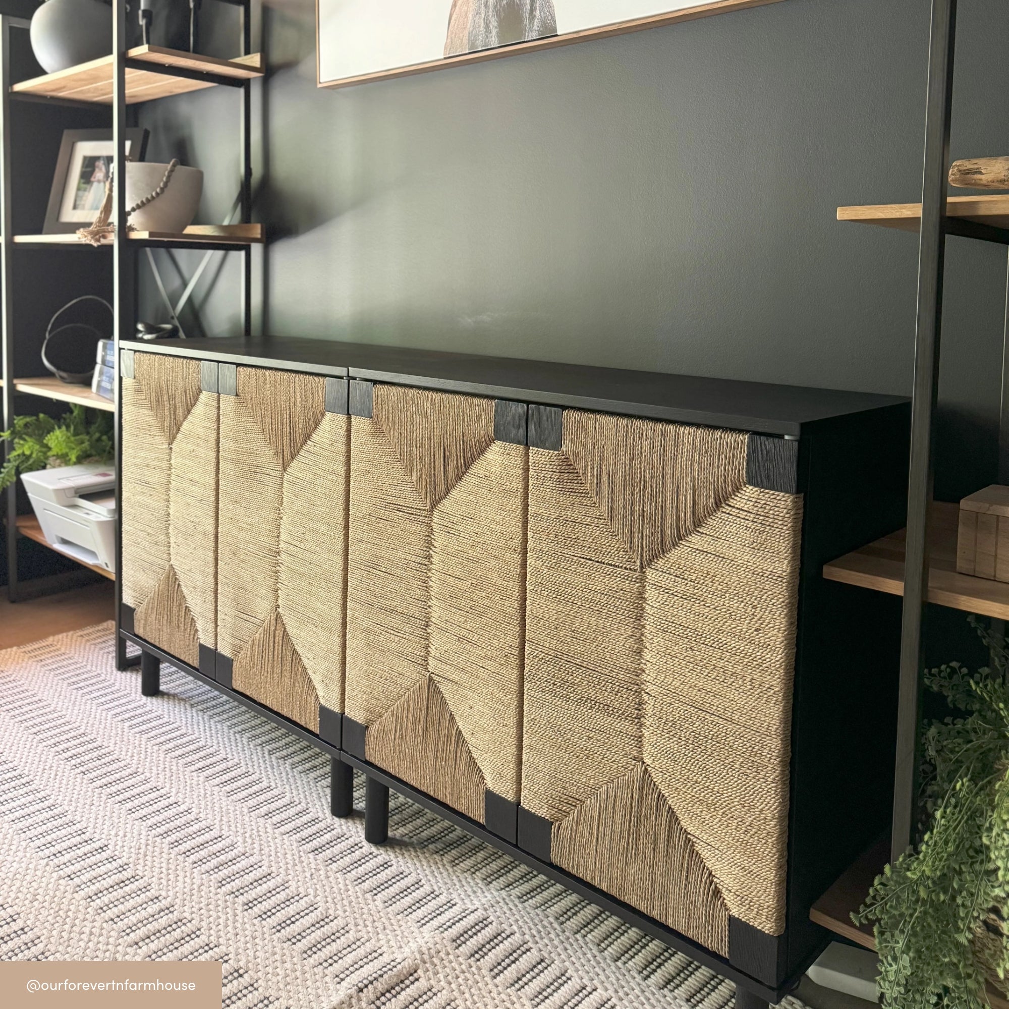 A modern black sideboard with four geometric woven rattan doors stands against a dark wall, flanked by wooden shelving units and decorated with plants and books.