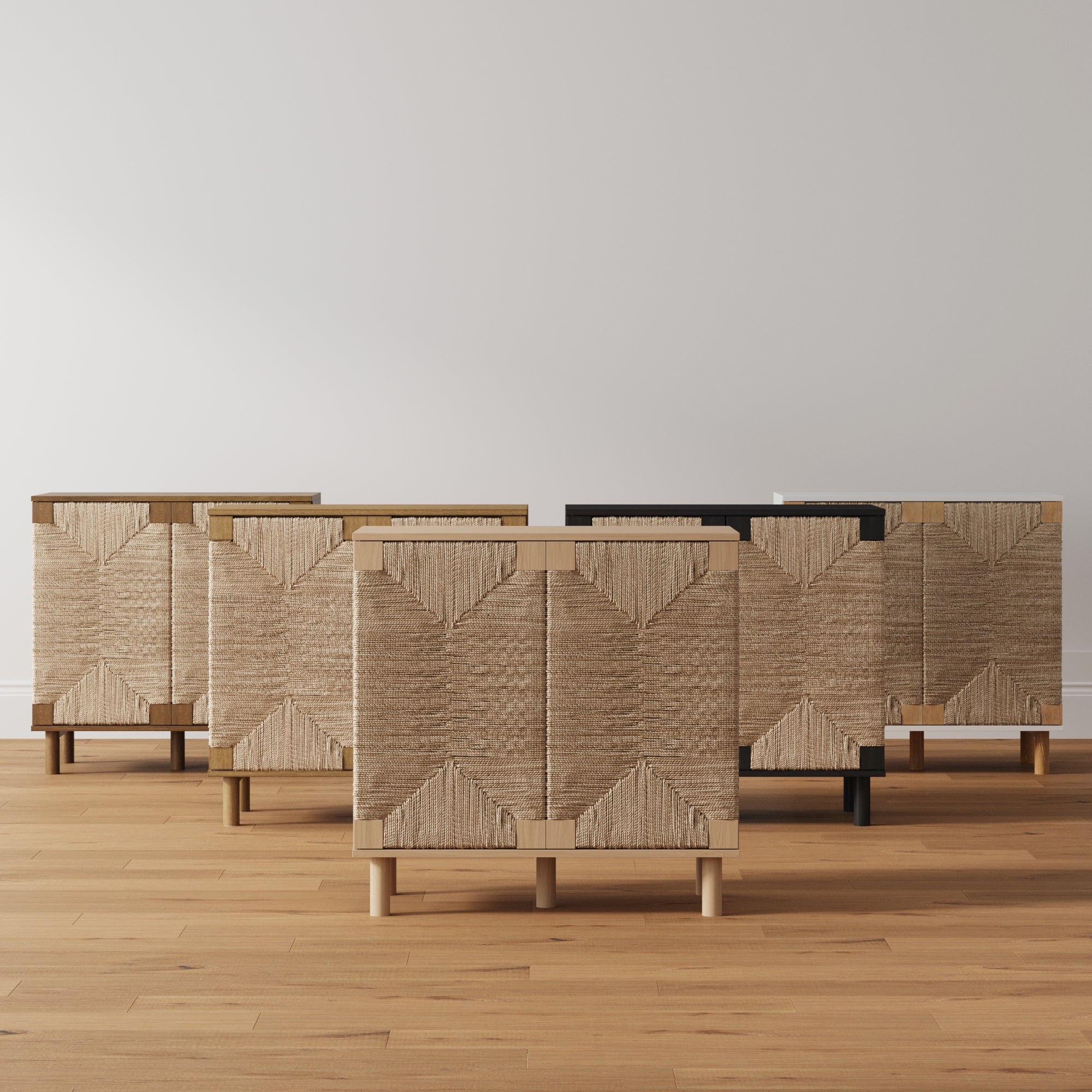 Five cabinets with woven textured doors and light wood frames are arranged in a row on a wooden floor against a plain white wall. The cabinets feature different leg finishes, including wood, brass, and black.