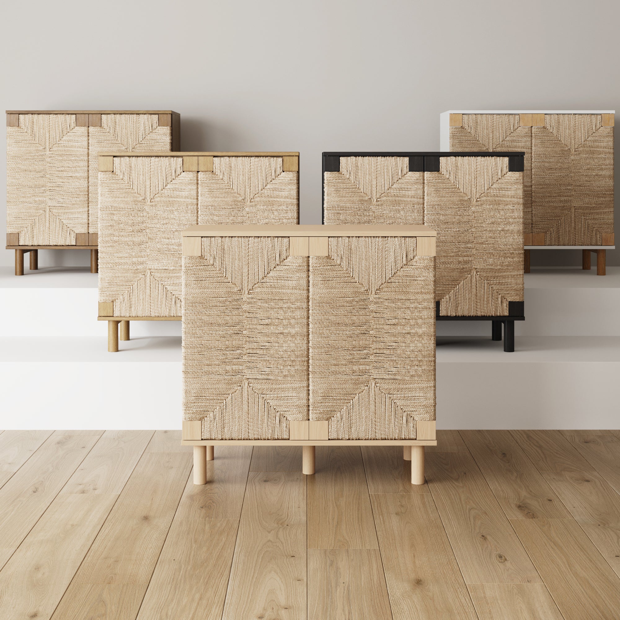 Five woven-front cabinets in various frame colors are displayed on white platforms against a neutral wall, with light wood flooring in the foreground. The cabinets feature geometric patterns on their doors.