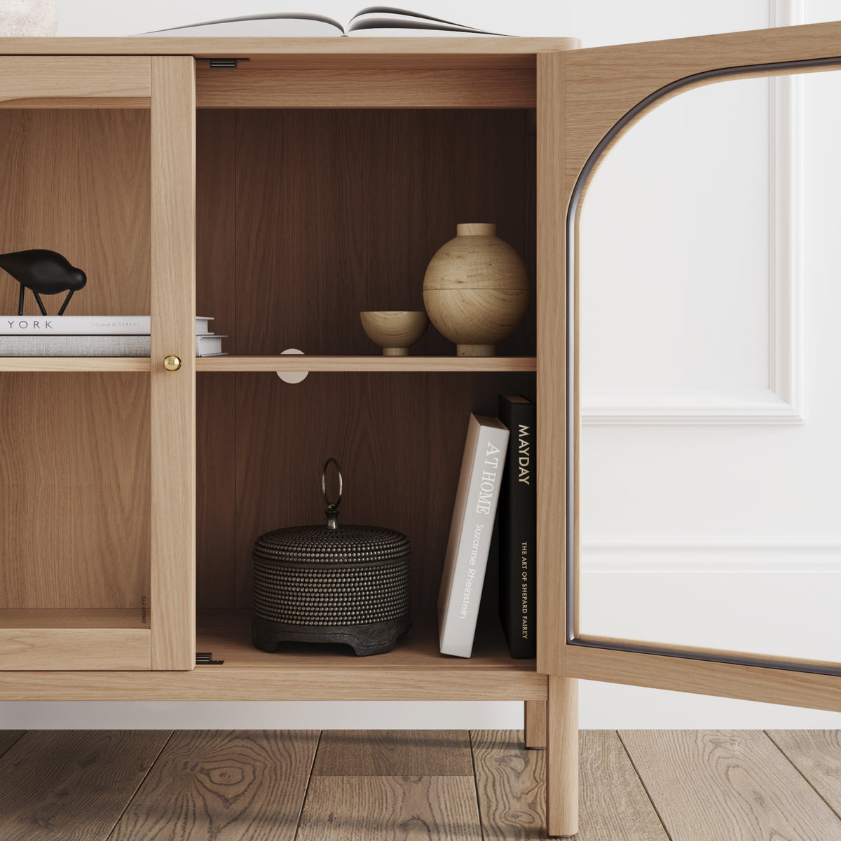 Large Glass Door Curio Cabinet Credenza Raw Oak with brass metal hardware and an open glass door revealing shelves styled with decorative objects and books.