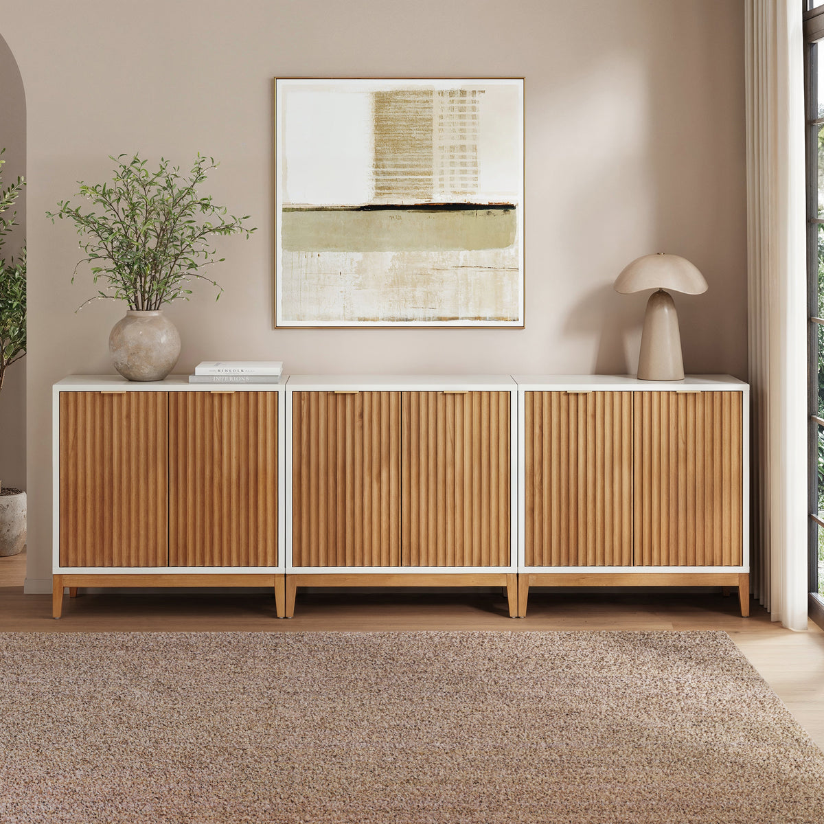 A set of three Nathan James Mid-Century Fluted Storage Credenza Warm White Warm Pine cabinets with white frames and fluted light-wood doors, arranged side-by-side against a wall.