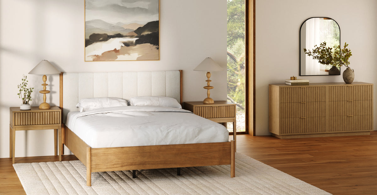 A modern bedroom featuring a light wood bed frame with an upholstered headboard, two matching wood nightstands with table lamps, and a wooden dresser with an arched mirror.